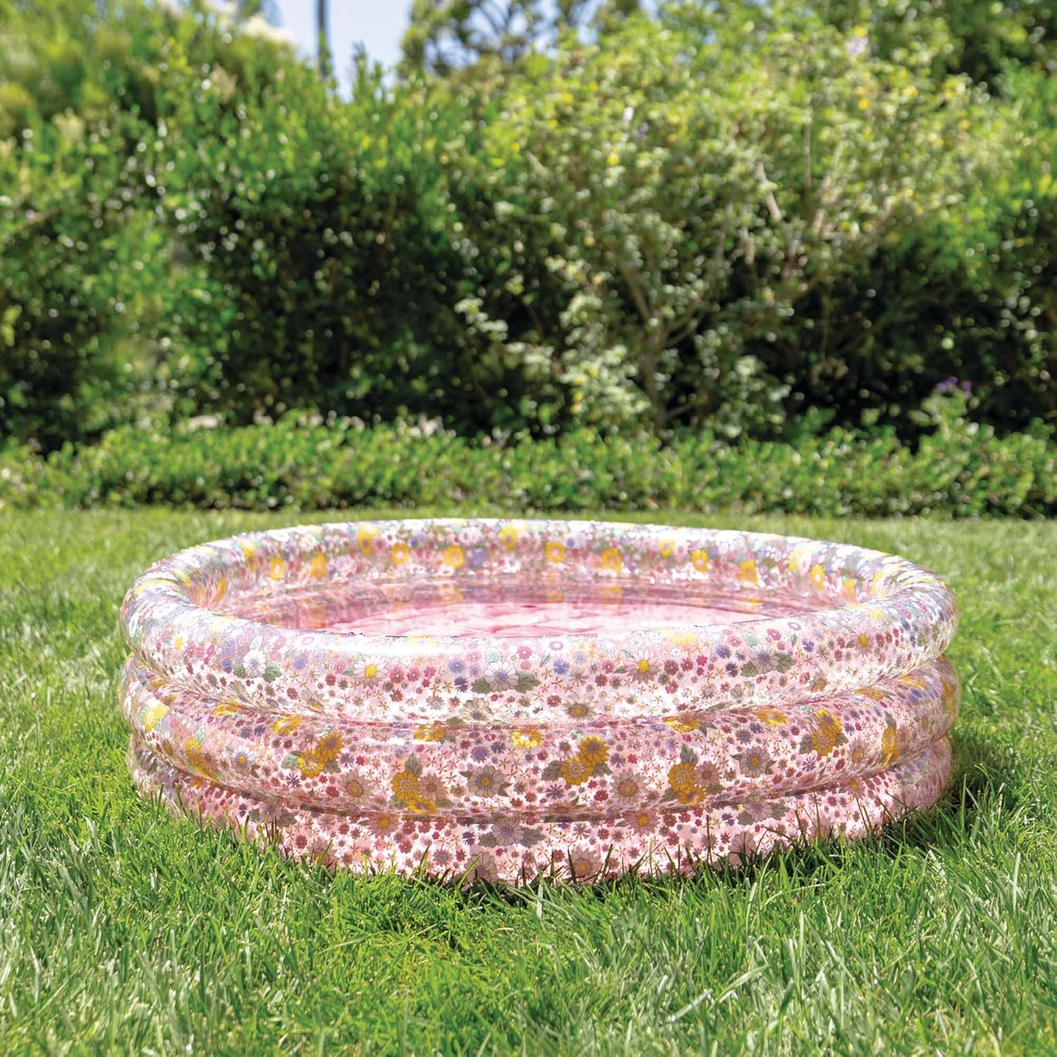 Różowy nadmuchiwany basen z kwiatowym wzorem na zielonym trawniku w słonecznej scenerii.