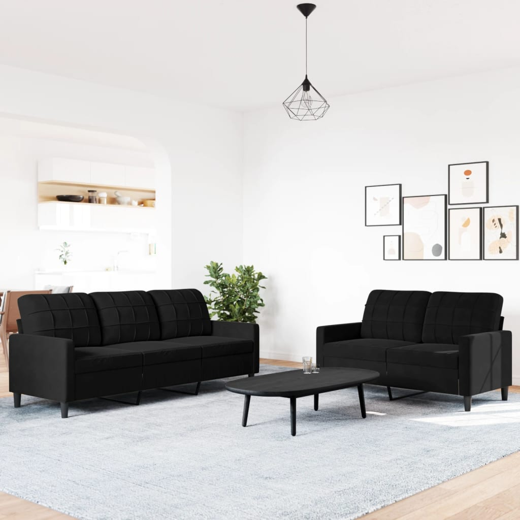 Wohnzimmer mit schwarzen Sofas, einem Couchtisch, einem Teppich und Wandkunst. Weiße Wände.