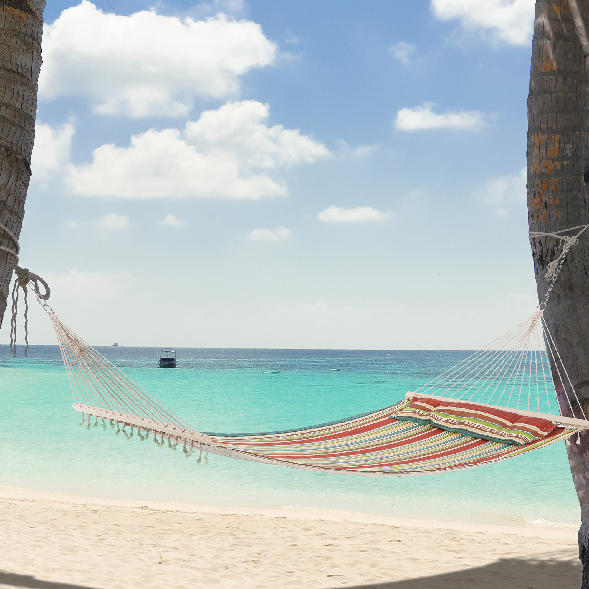 Hängematte zwischen Palmen an einem Strand mit türkisfarbenem Wasser und blauem Himmel mit Wolken.