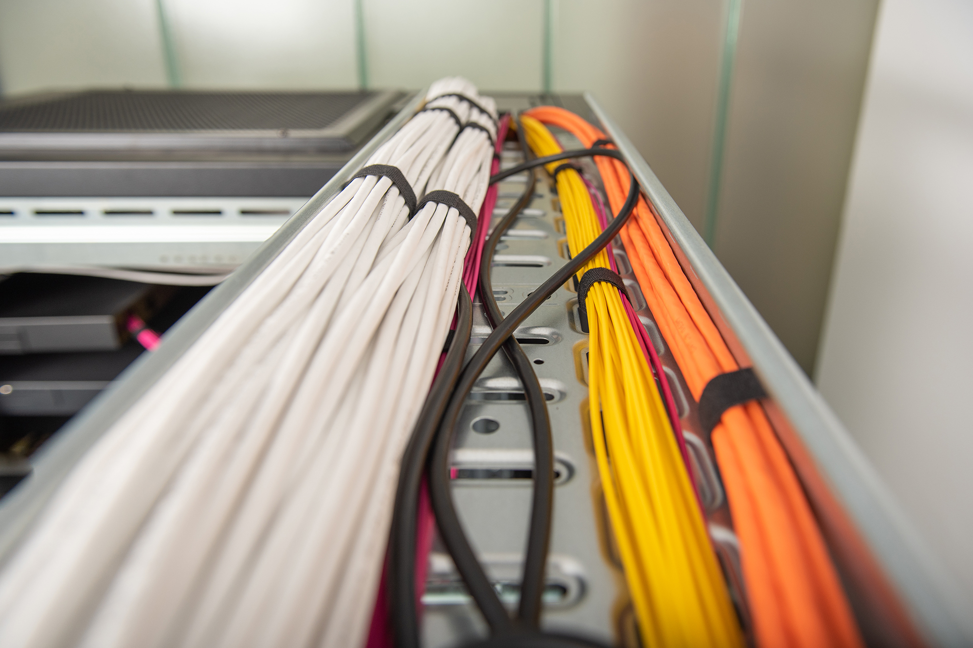 Das Bild zeigt Bündel farbiger Netzwerkkabel in einem Server. Die Kabel sind weiß, gelb und orange.