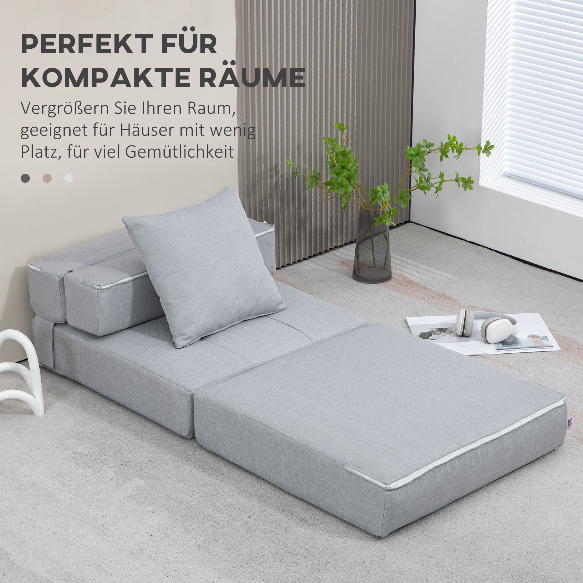 Graues Modulsofa auf hellem Teppich. Ein graues Kissen liegt auf dem Sofa. Im Hintergrund eine Vase mit einer grünen Pflanze.