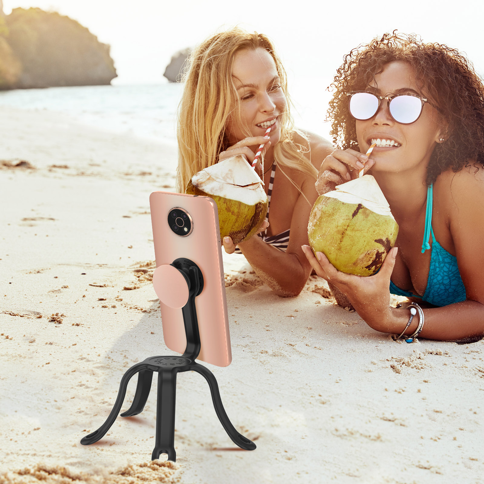 Due donne sulla spiaggia, bevono da noci di cocco, usano un telefono su un treppiede.
