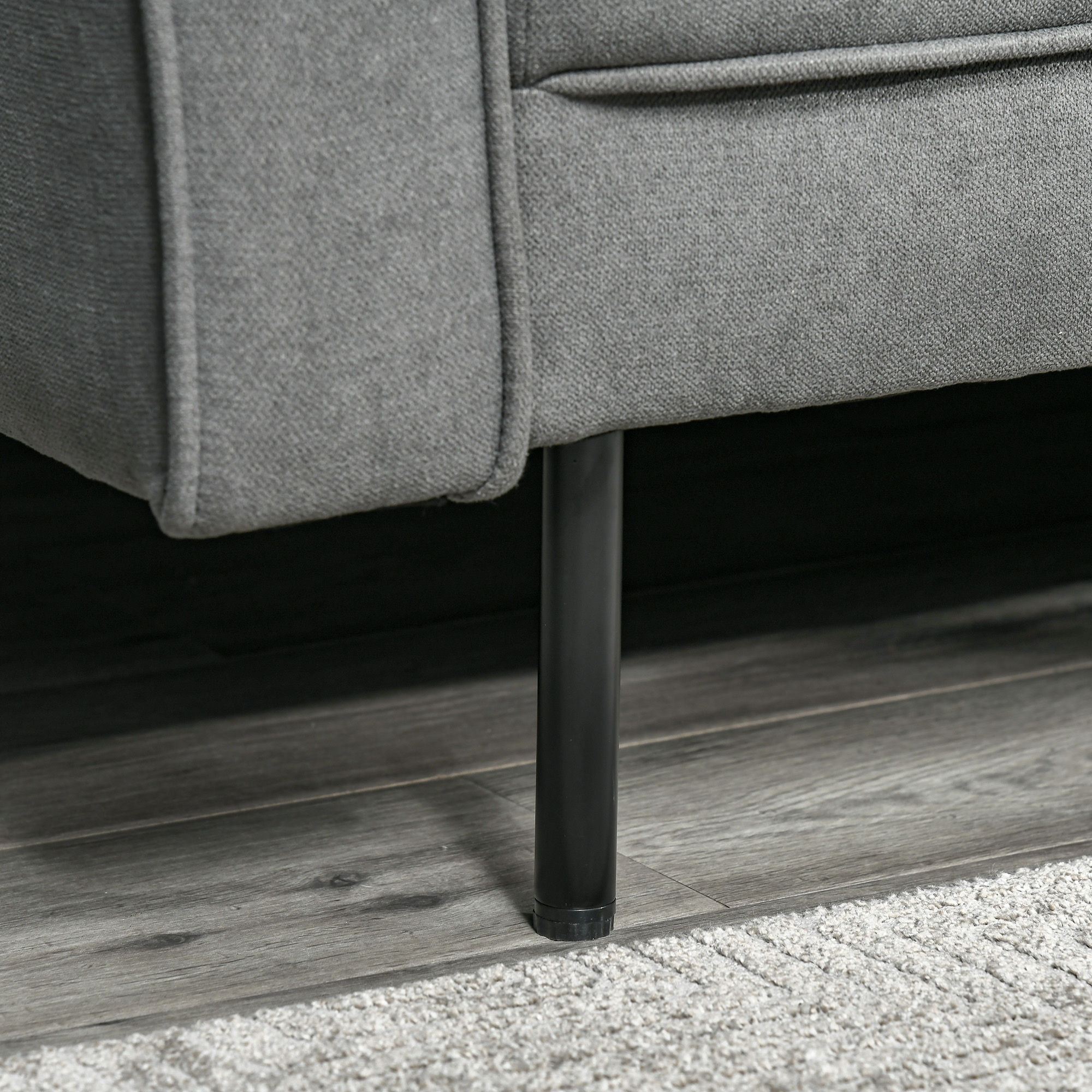 Nahaufnahme des Beins eines grauen Sofas, zeigt das schwarze zylindrische Bein und den Teppich.