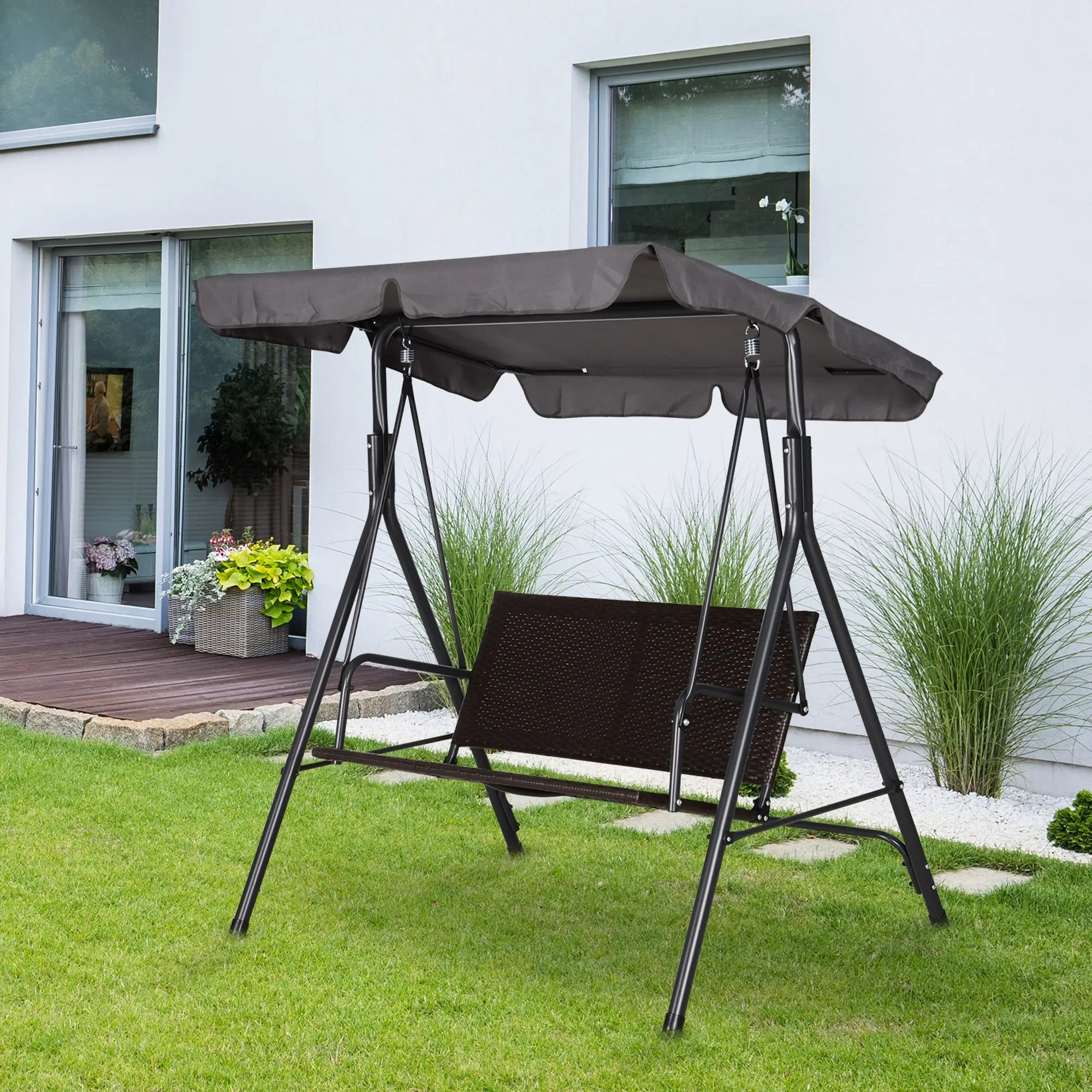 Schaukel mit Baldachin im Freien auf einem grünen Rasen. Haus und Pflanzen im Hintergrund.