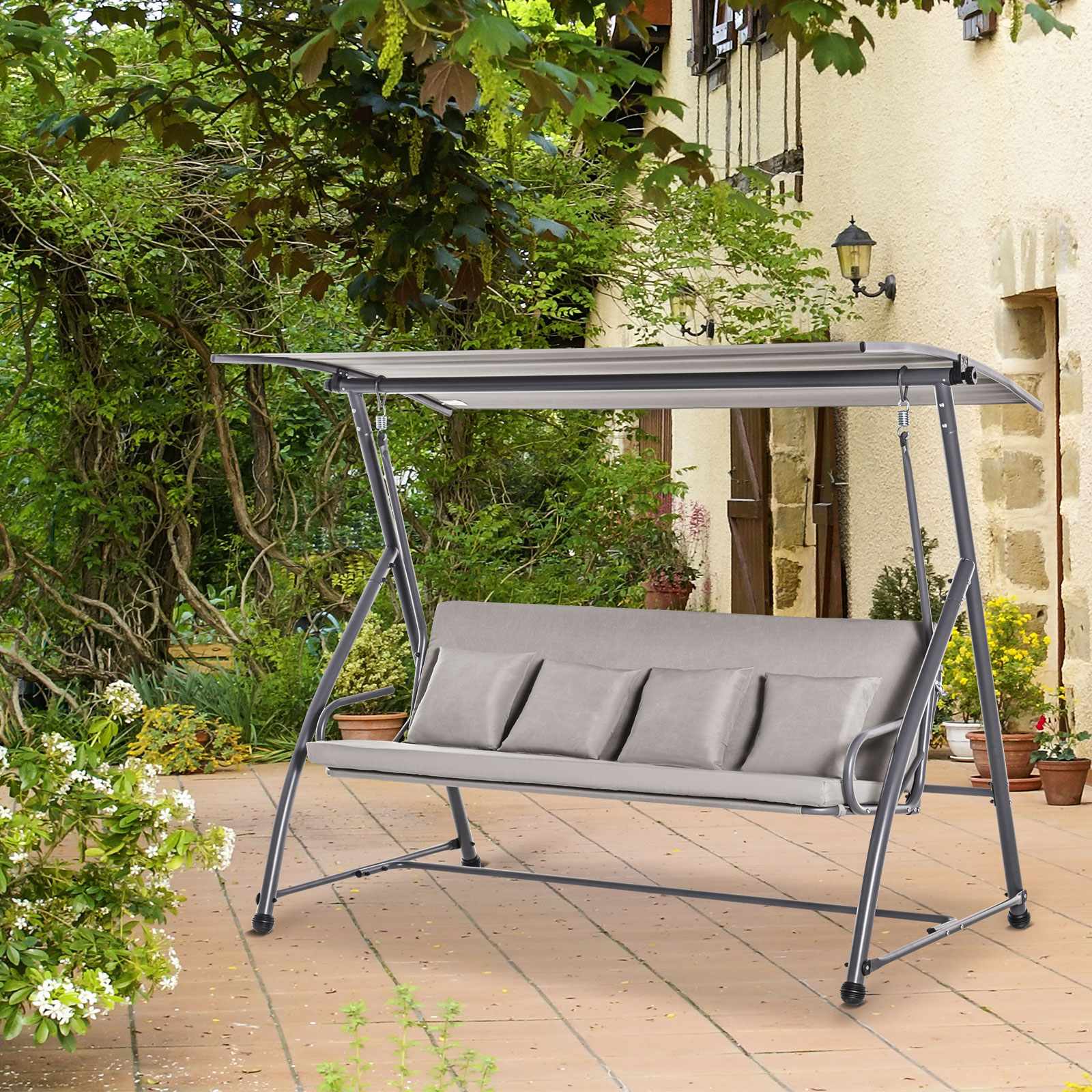 Graue Schaukel mit Sonnensegel in einer Gartenumgebung mit Pflanzen und einem Haus.