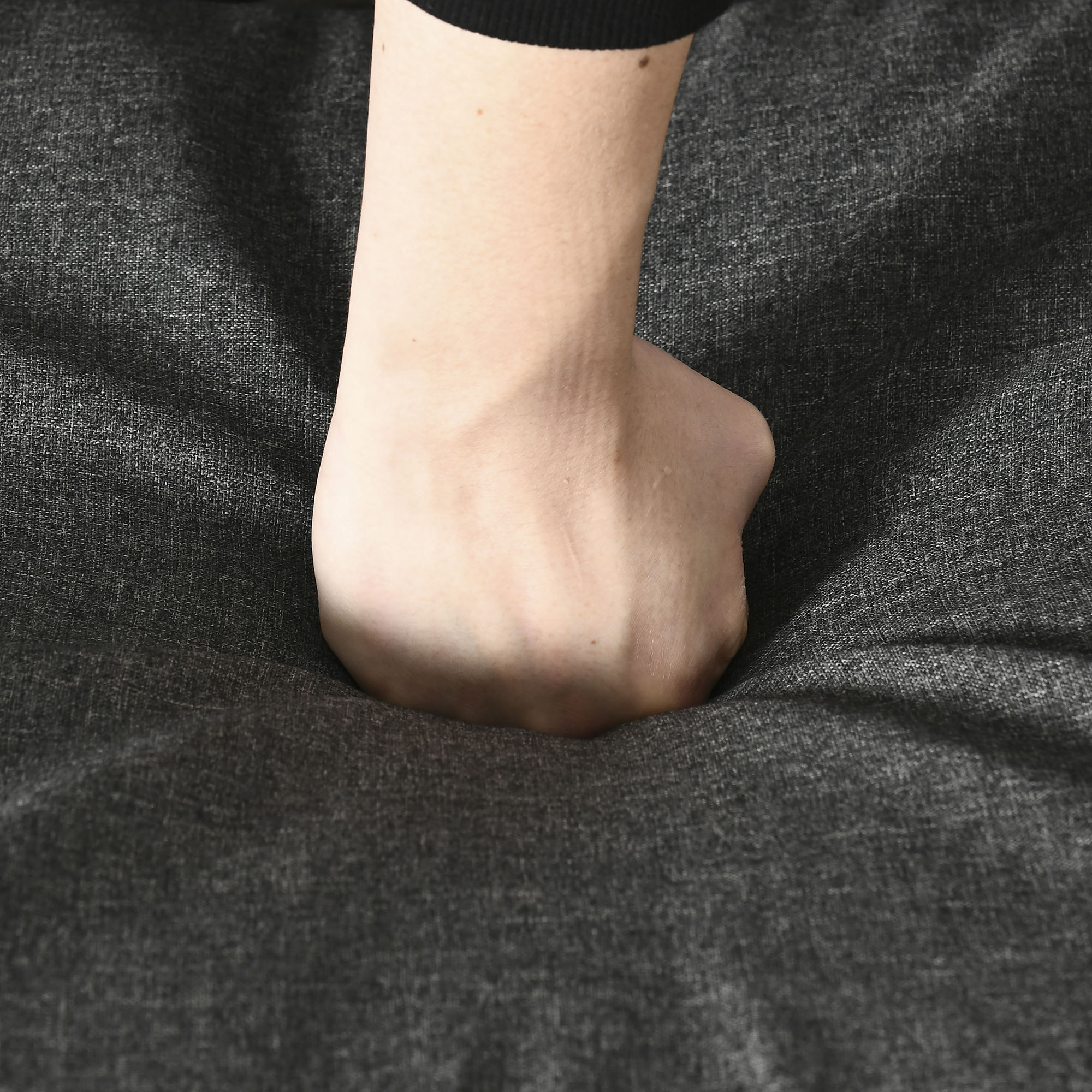 Hand drückt in eine dunkelgraue gepolsterte Oberfläche.