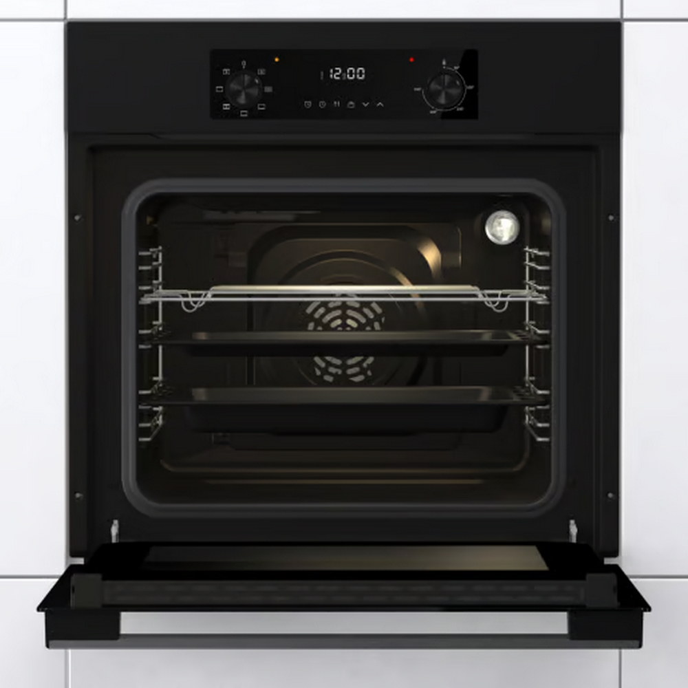 Forno nero aperto con vassoi all'interno, display digitale in alto, su parete bianca.