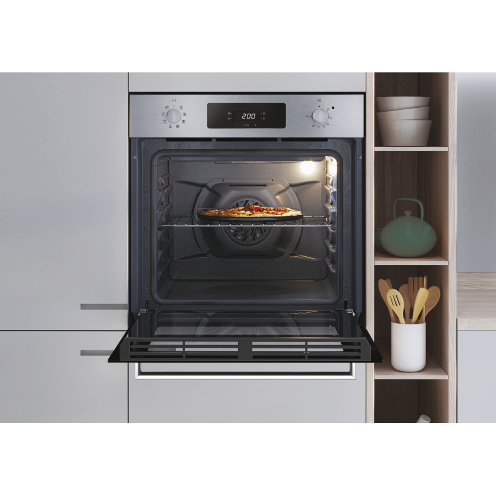 Un forno con una pizza all'interno, la porta è aperta. Ci sono mensole con utensili da cucina a destra.