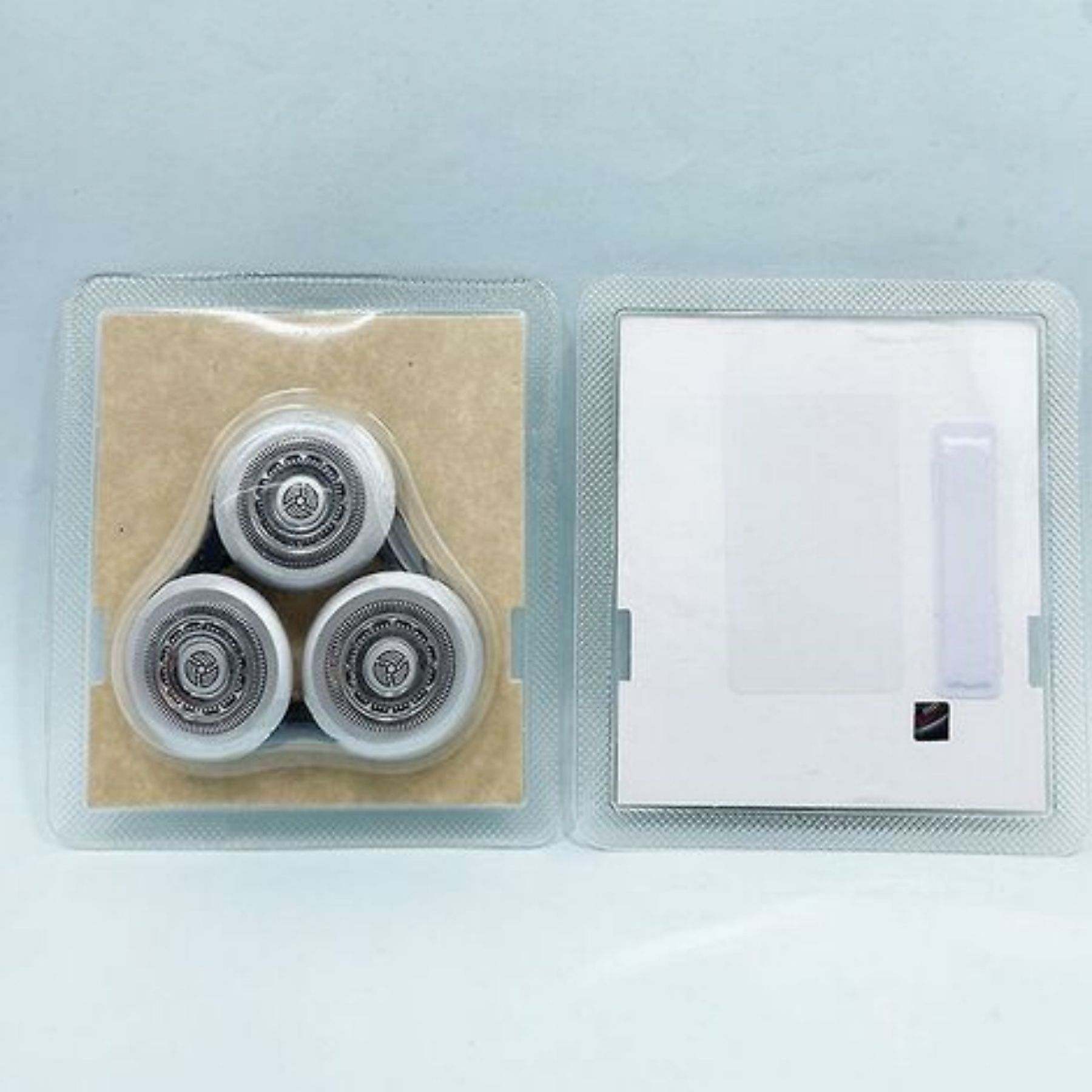 Drei silberne, kreisförmige Rasierköpfe in einer transparenten Kunststoffverpackung auf weißem Grund.