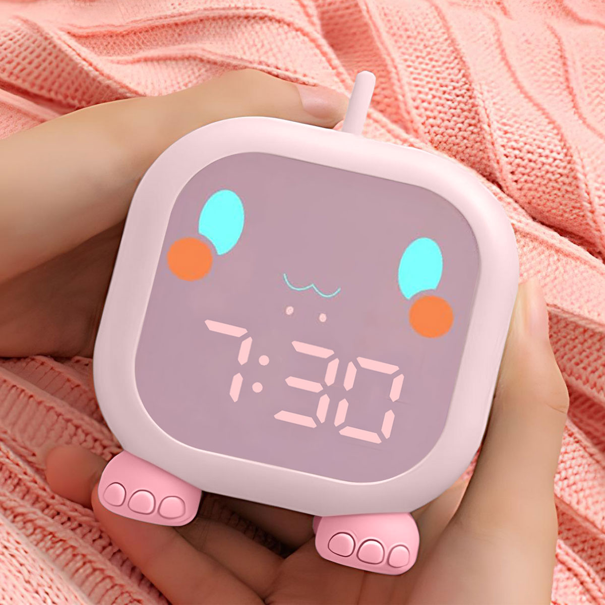 Un despertador rosa con una cara de dibujos animados. Muestra las 7:30 en la pantalla, sostenido por manos.