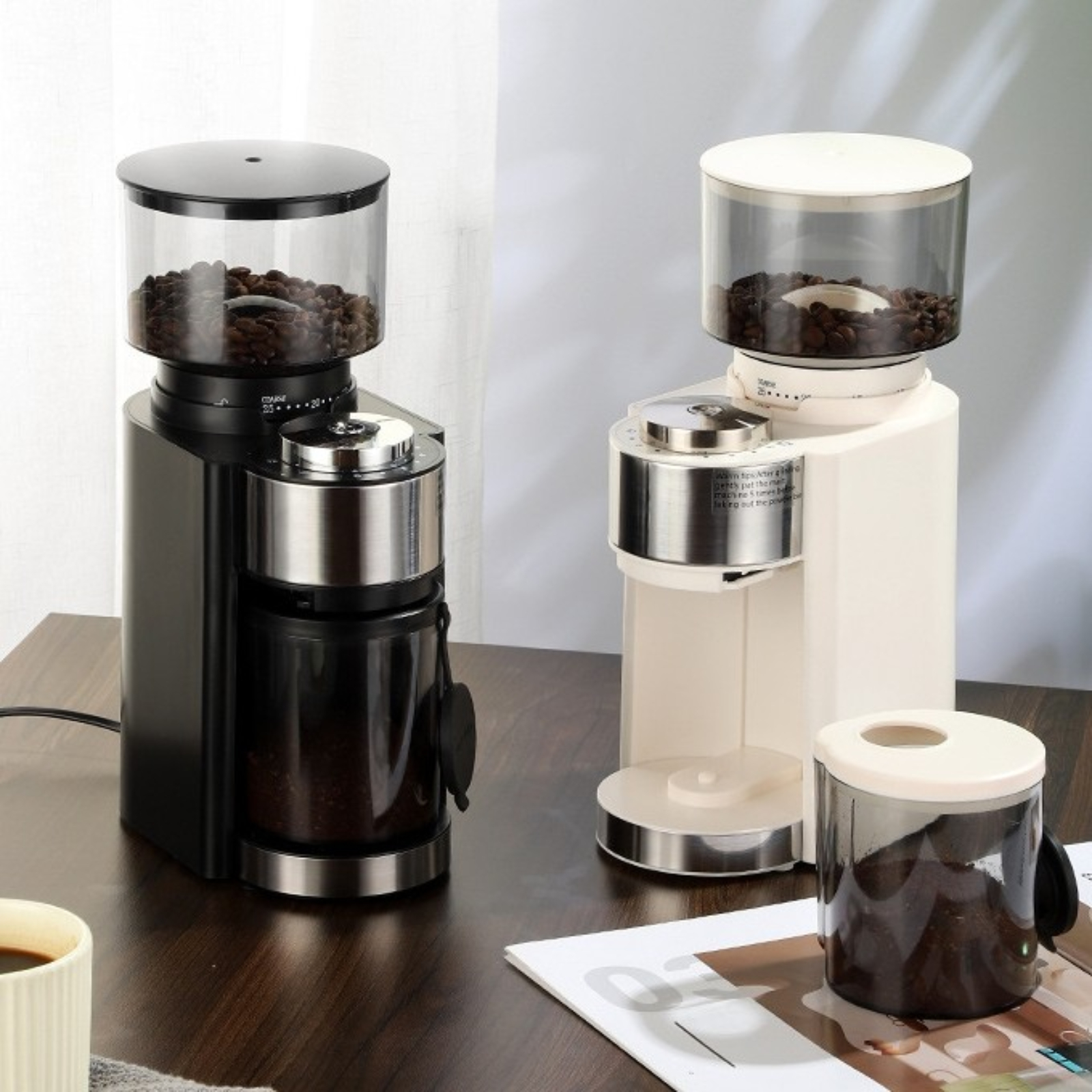 Zwei Kaffeemühlen, eine schwarz, eine weiß, mit Kaffeebohnen im Behälter.