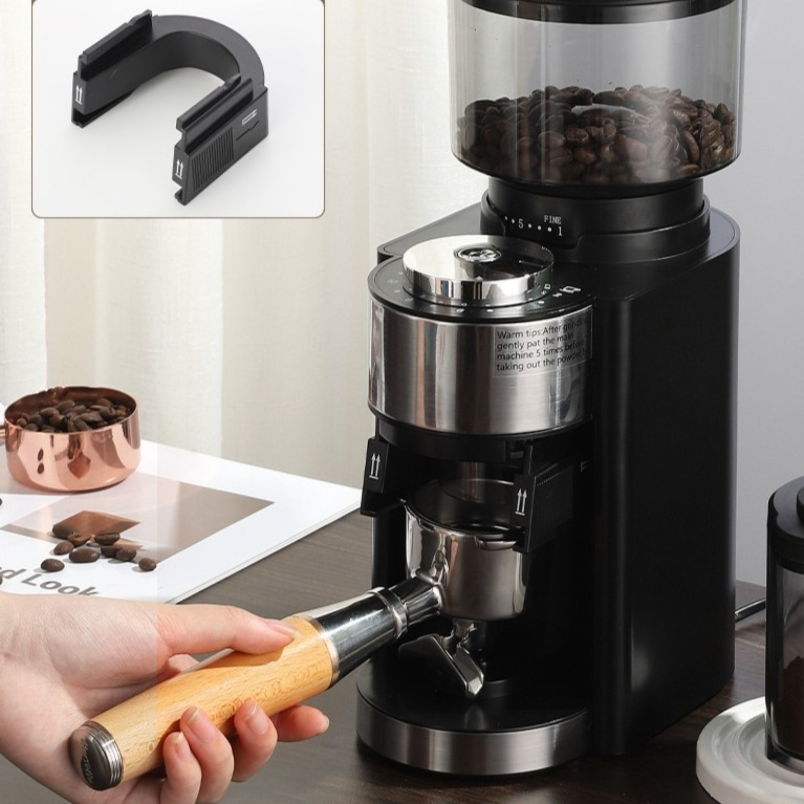 Eine schwarze Kaffeemühle mit Holzgriff, eine Hand, die den Griff hält, und eine Kupferschale. Kaffeebohnen oben.