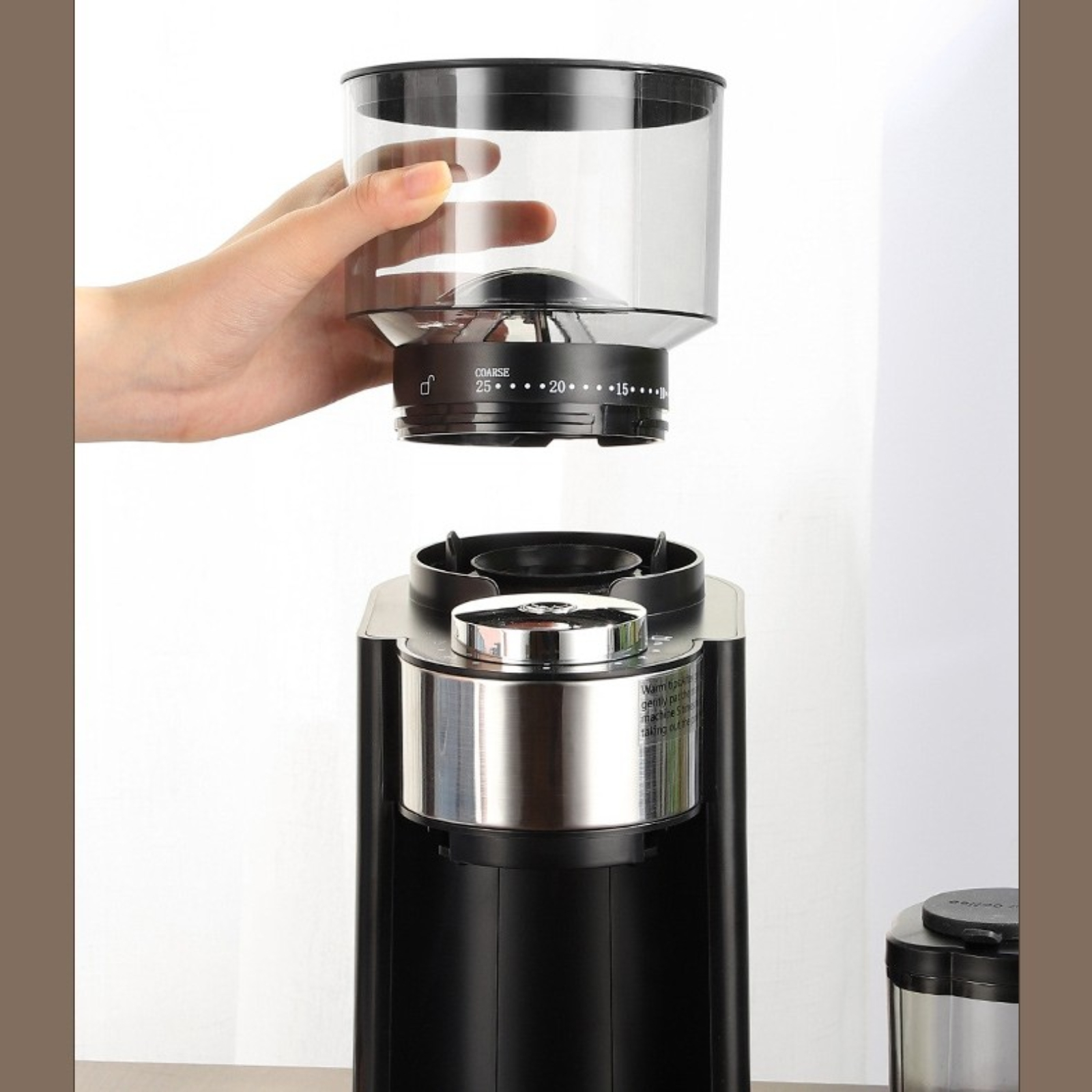 Eine Hand, die Kaffeebohnen in eine schwarze Kaffeemühle mit einem transparenten Behälter schüttet.