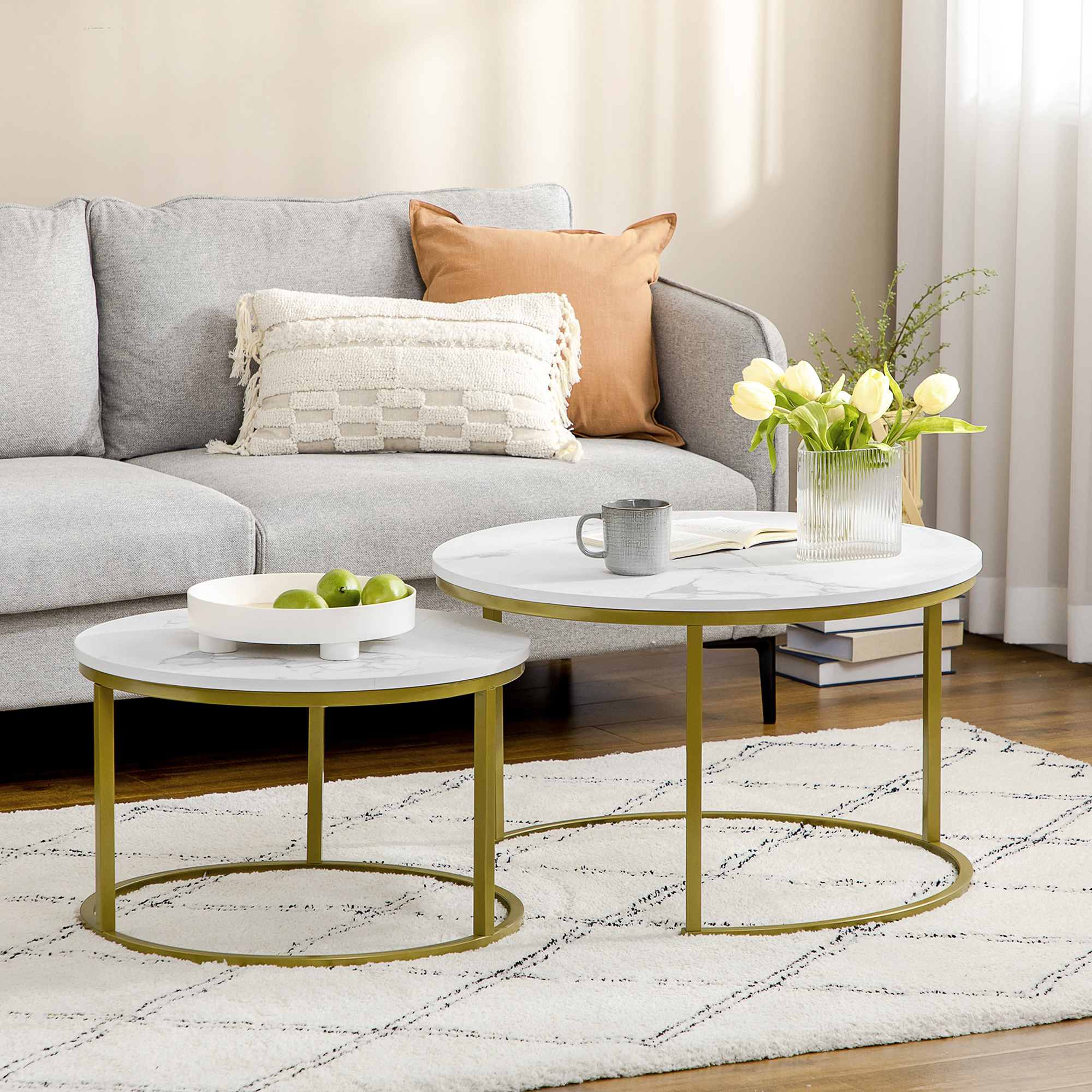 Zwei weiße Couchtische mit Marmorplatte und goldenen Rahmen, neben Sofa und Teppich.