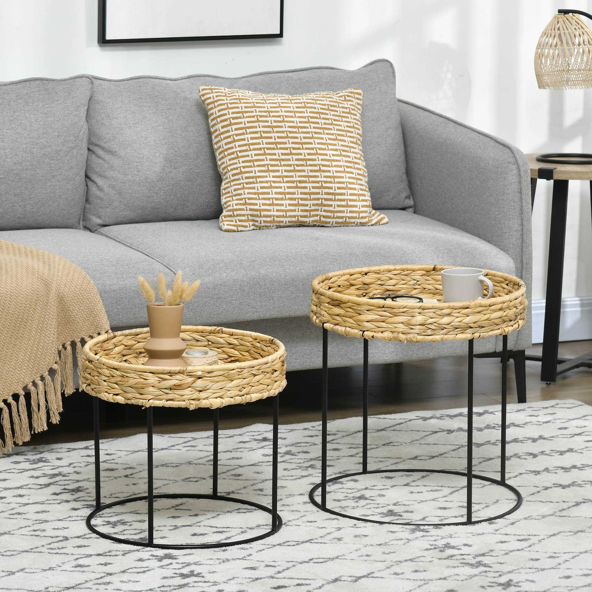 Zwei Beistelltische aus Korbgeflecht mit schwarzen Metallbeinen, auf einem Teppich, Sofa im Hintergrund.