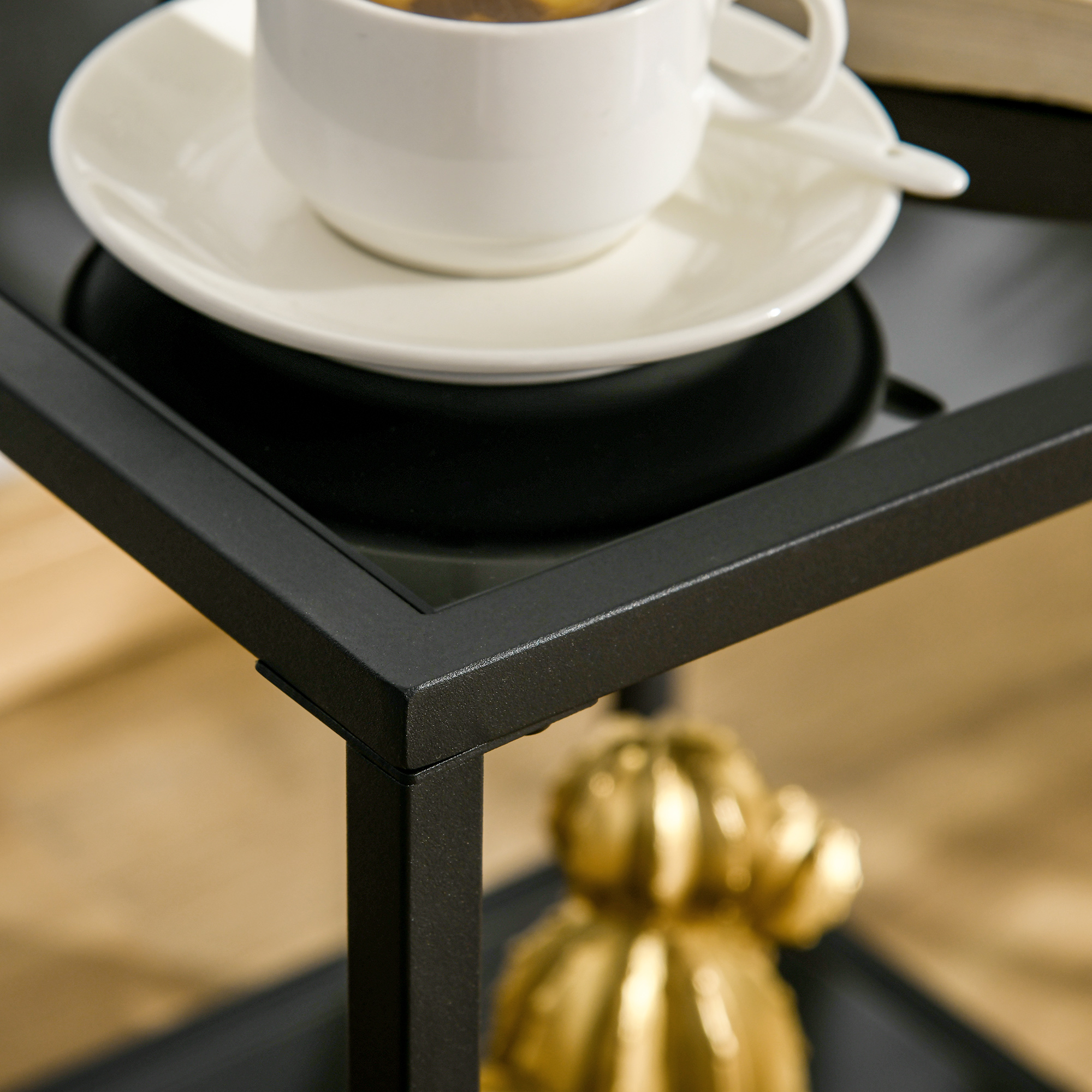 Nahaufnahme eines schwarzen Tisches mit einer weißen Tasse und Untertasse sowie einer goldenen Kaktusdekoration.