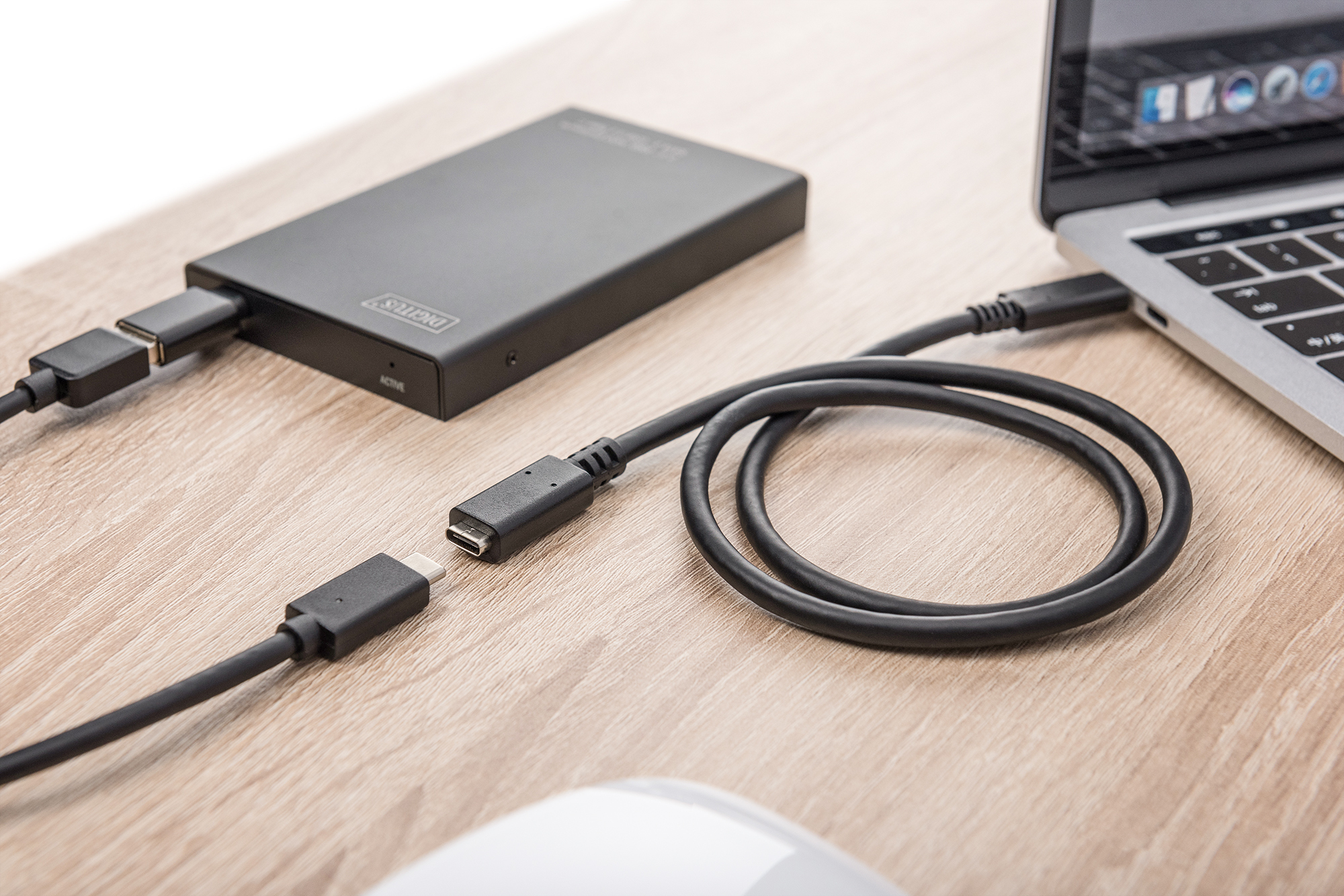 Schwarze externe Festplatte, verbunden mit Laptop mit schwarzem USB-Kabel auf hellem Holztisch.