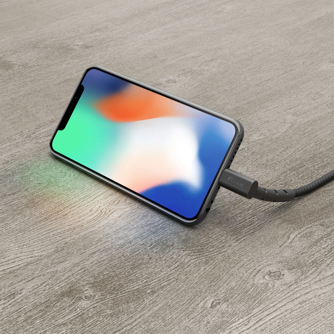 Telefon lädt auf Holzoberfläche. Der Bildschirm ist bunt. Ein Ladekabel ist eingesteckt.