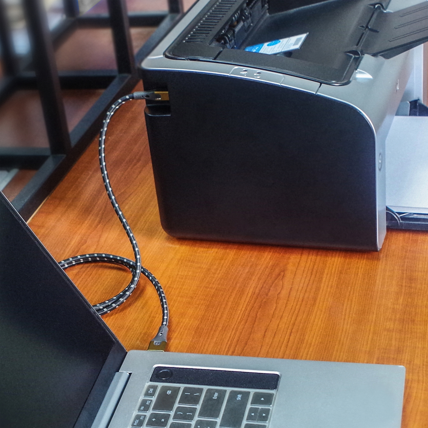 Laptop mit Drucker mit Kabel verbunden. Beide stehen auf einem Holztisch.