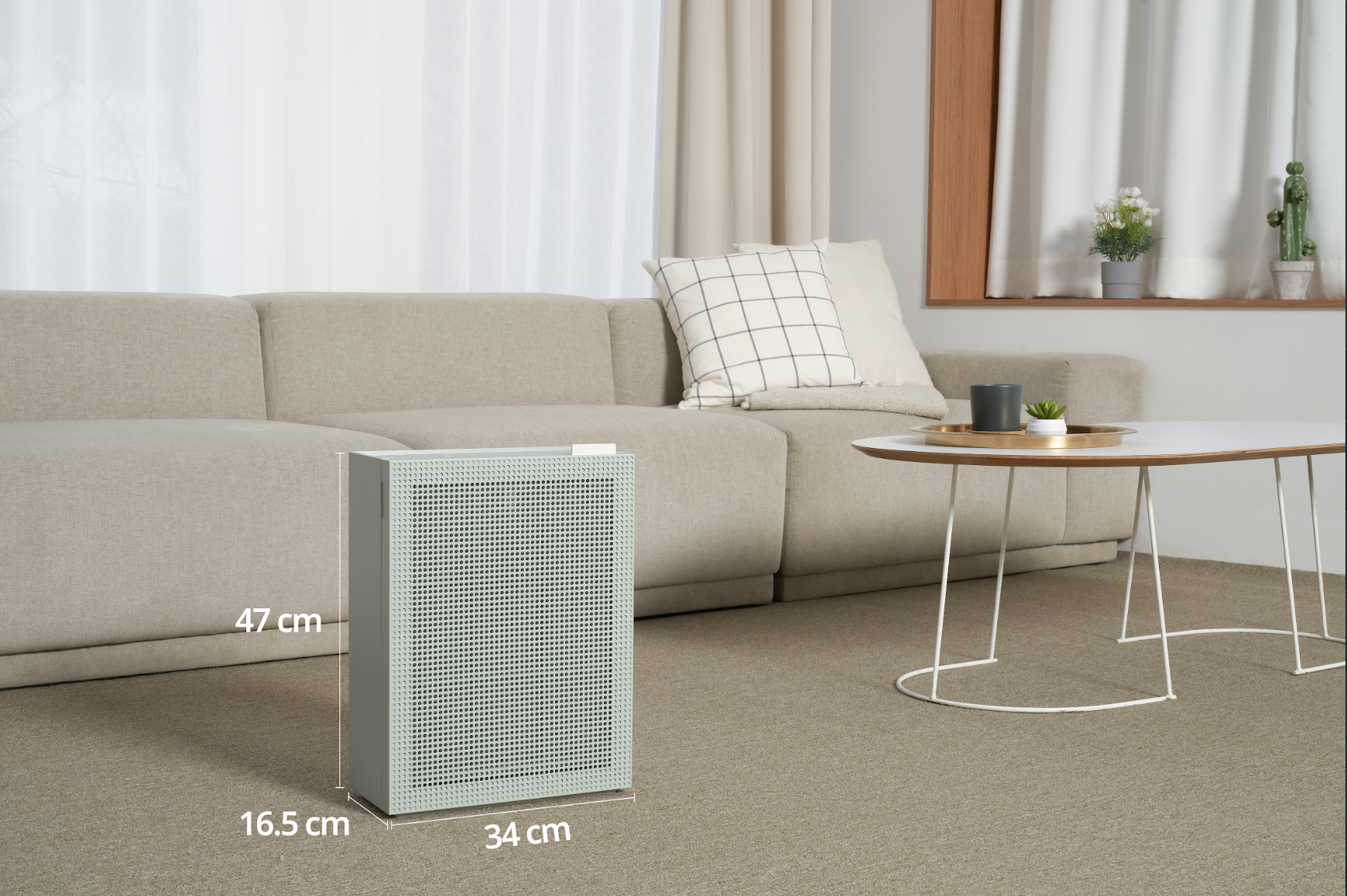 Luftreiniger im Wohnzimmer, grün-grau, mit Abmessungen, in der Nähe einer Couch und eines Tisches.