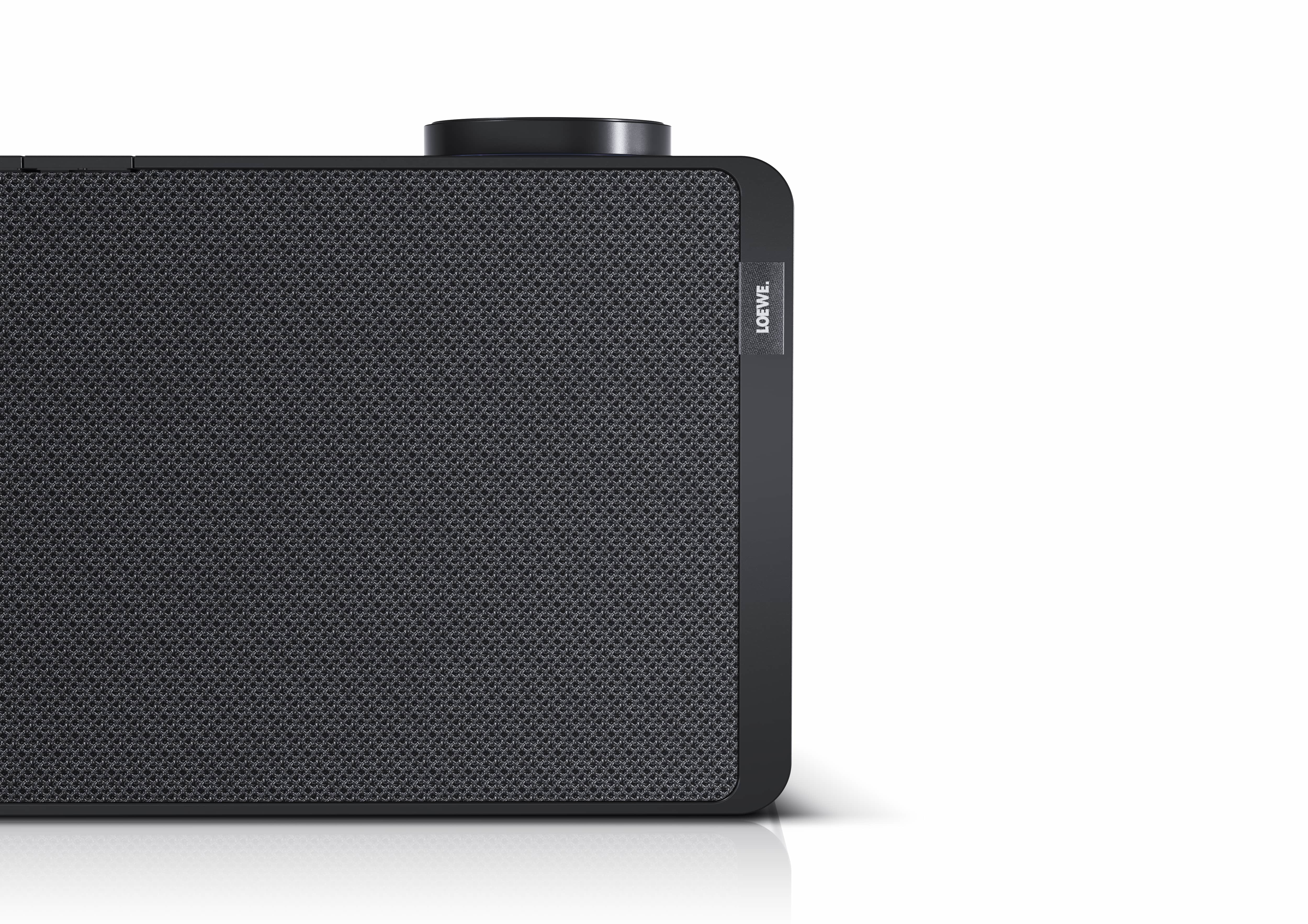 Czarny głośnik z siatkowym przodem i etykietą Loewe. Prawa strona na białym tle.