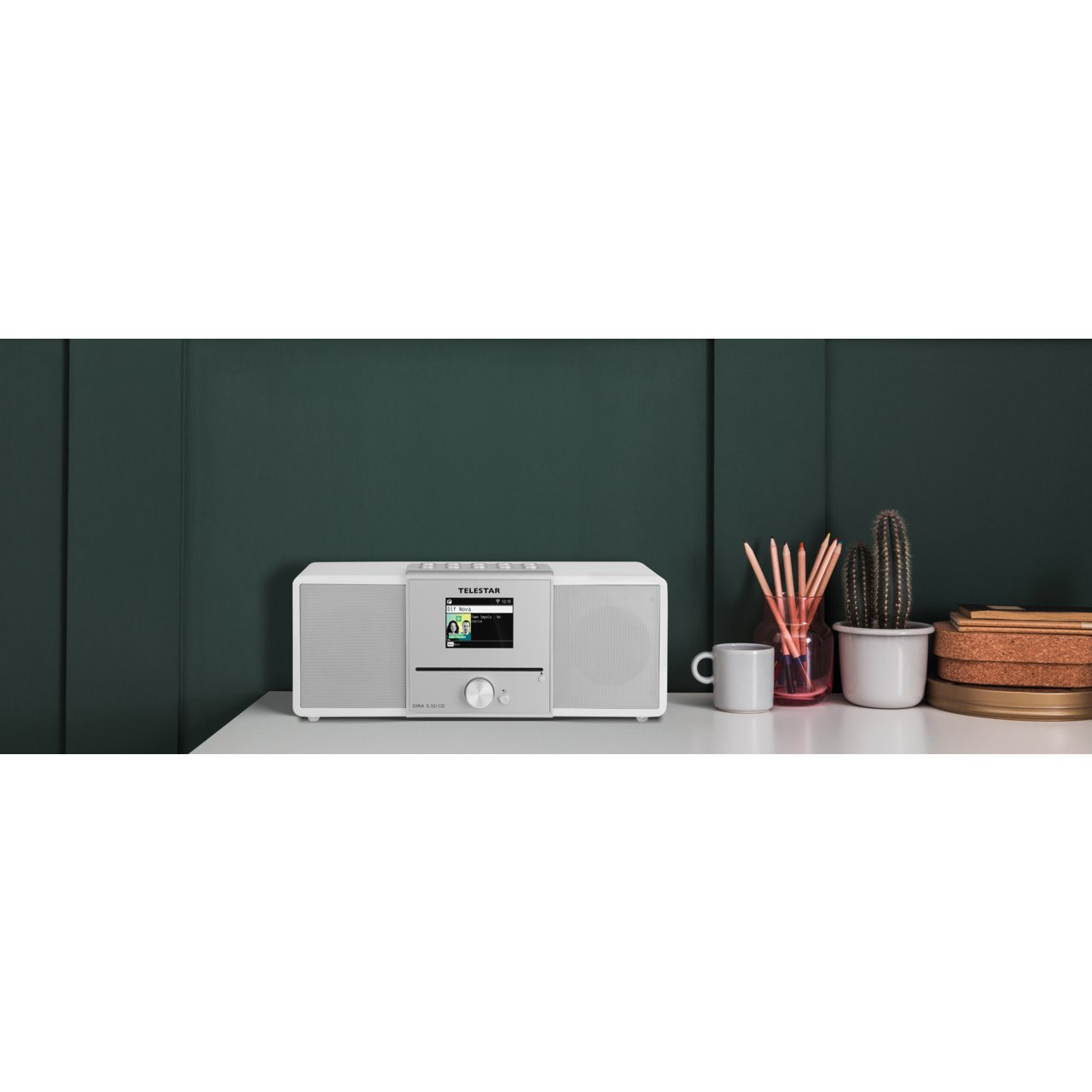 Białe stereo z ekranem, ołówkami i rośliną na półce z ciemnym tłem.