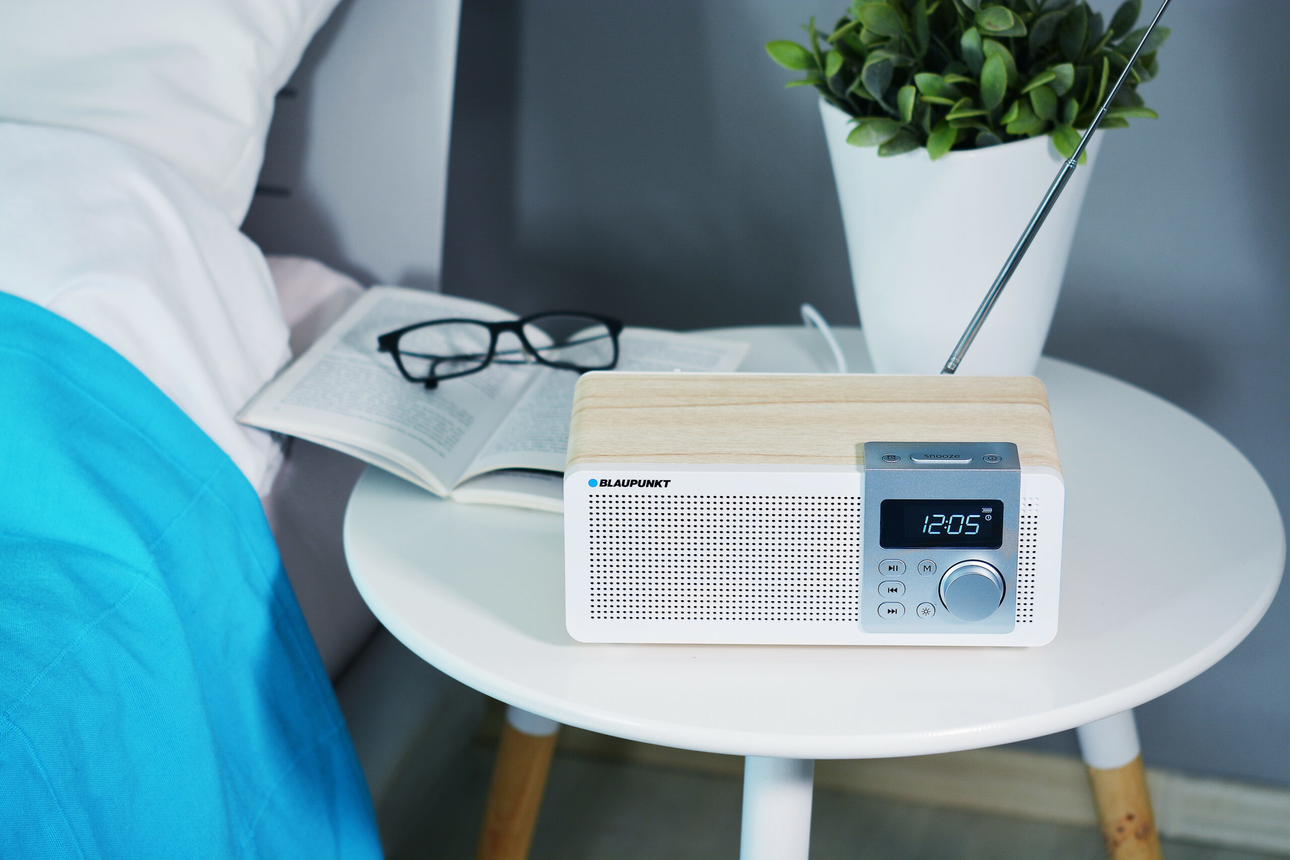 Radio digitale effetto legno accanto a libro e occhiali su comodino.