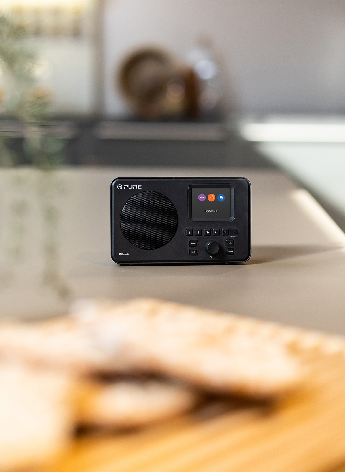 Schwarzes Digitalradio mit Bildschirm, Knöpfen und Lautsprecher auf einem hellen Tisch.