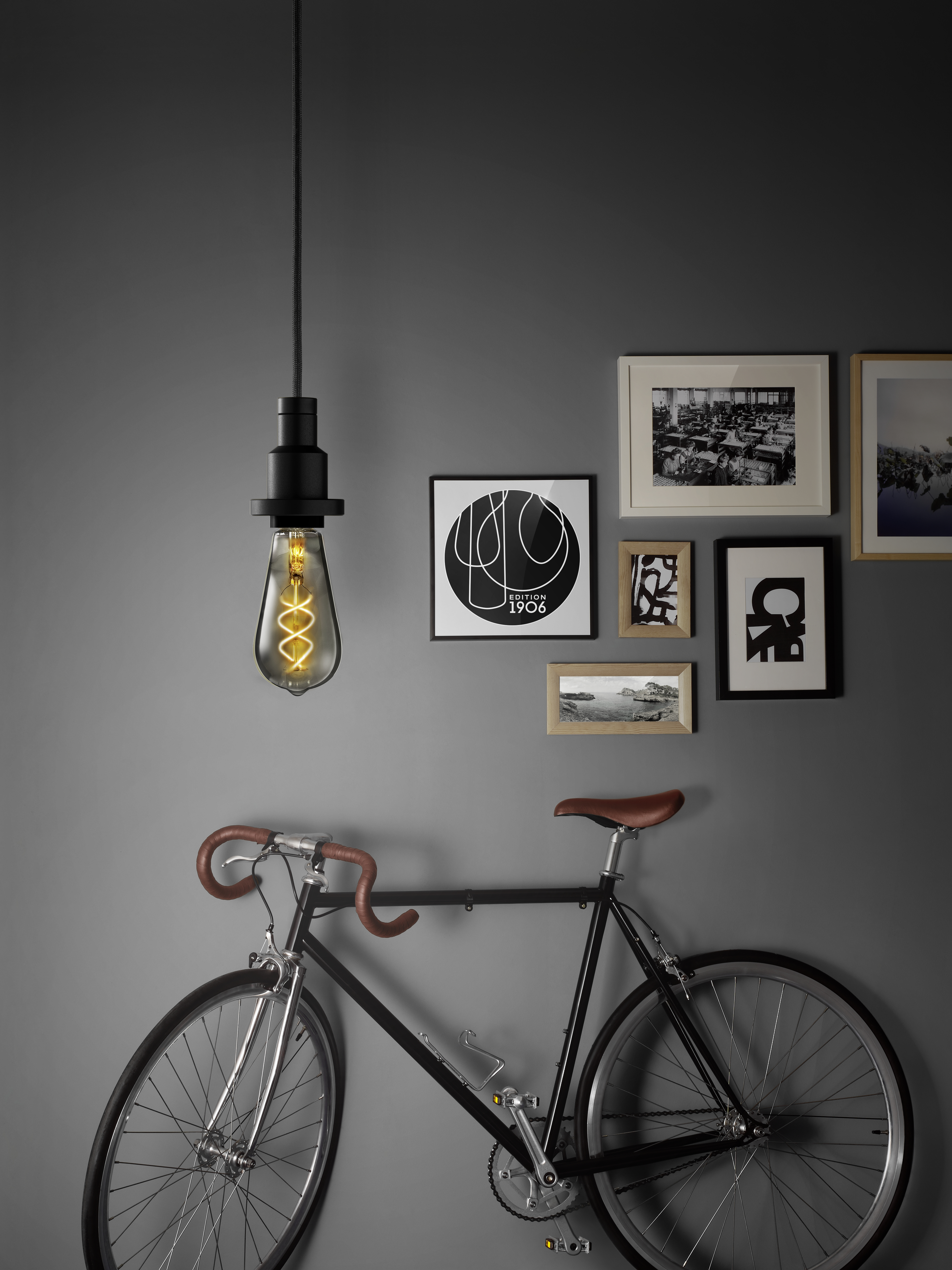 Schwarzes Fahrrad lehnt an grauer Wand, mit Bildern und Glühbirne.
