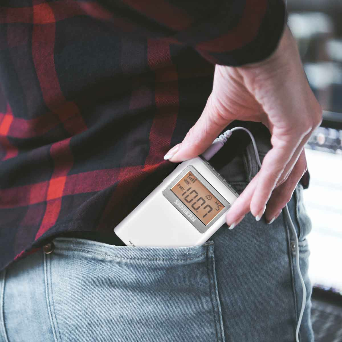 Osoba trzymająca białe radio cyfrowe w kieszeni. Widoczna koszula i dżinsy.