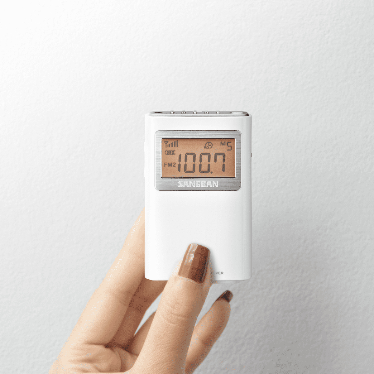 Białe radio z cyfrowym wyświetlaczem, trzymane w dłoni z brązowym paznokciem.