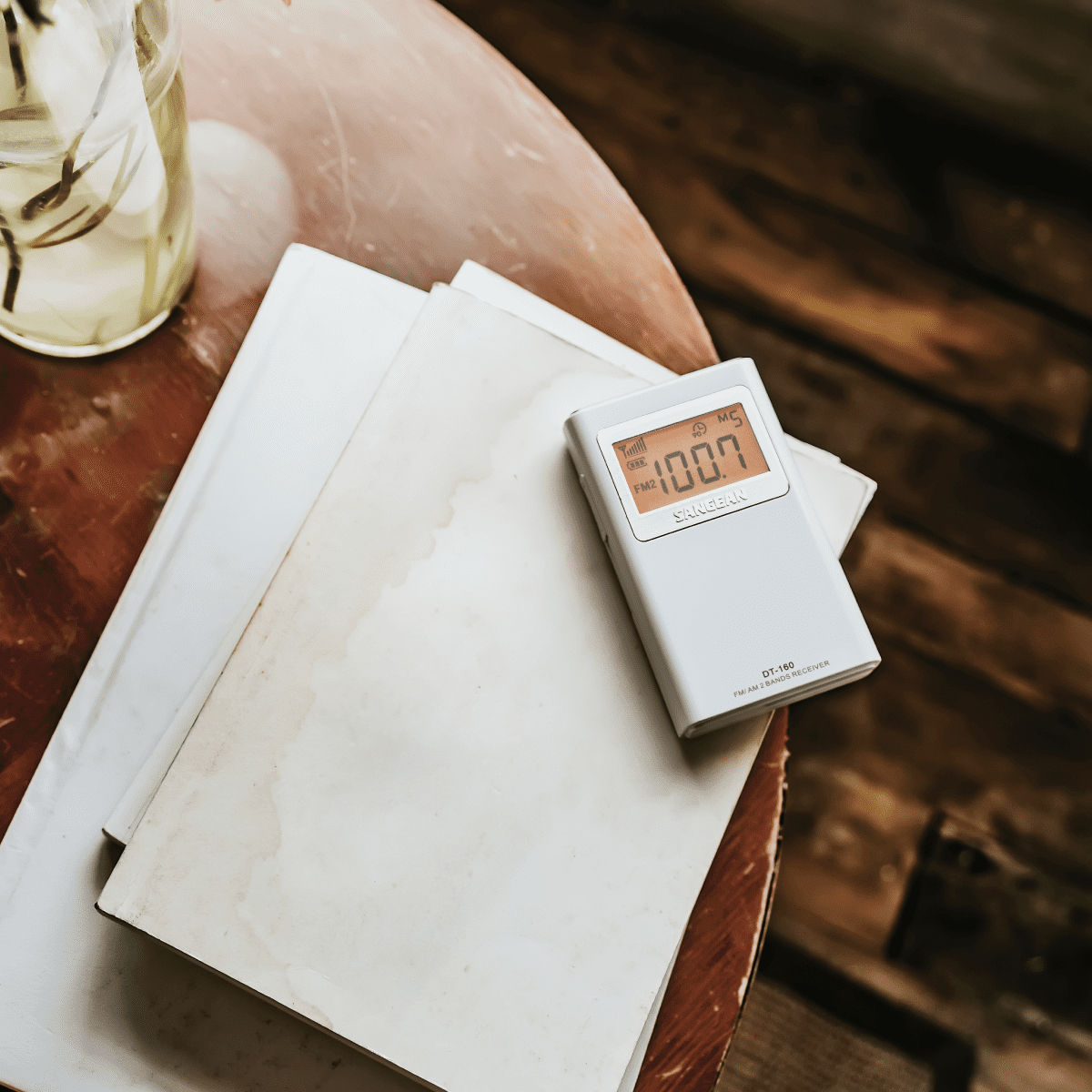 Białe radio z wyświetlaczem cyfrowym, na stole z książkami. Tło jest rozmyte.