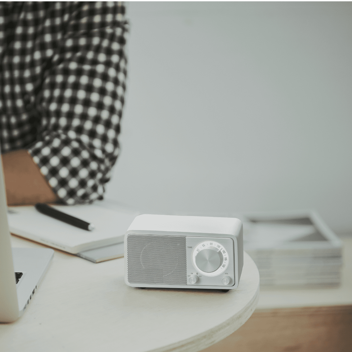 Małe, biało-szare radio z okrągłą tarczą i kratką głośnika, na stole.