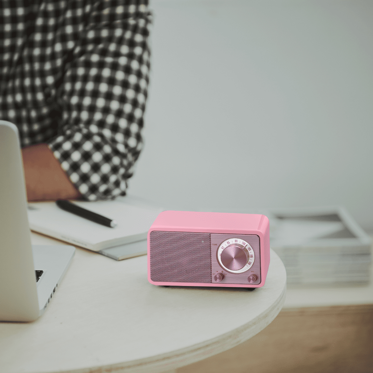 Różowe radio na białym stole. Osoba w koszuli w kratę w tle.