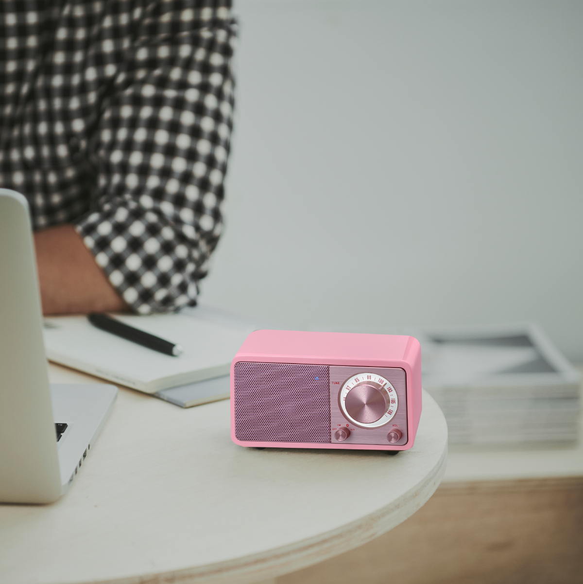 Różowe radio retro na białym stole. Obok osoba pracuje na laptopie.