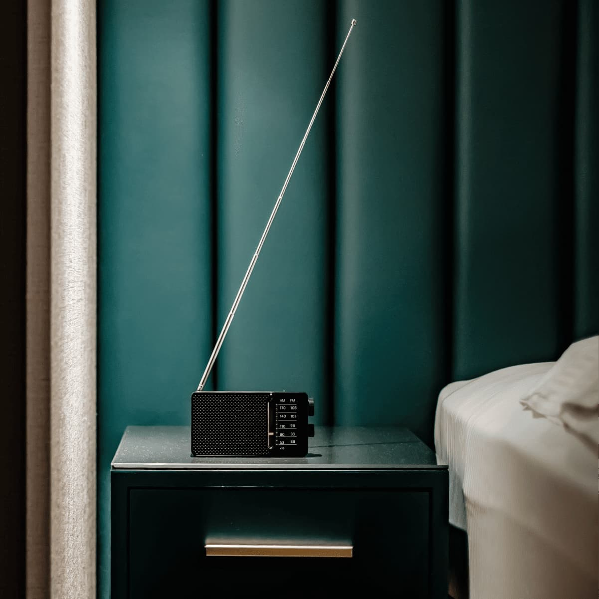 Małe, czarne, retro radio stoi na ciemnym stoliku nocnym.