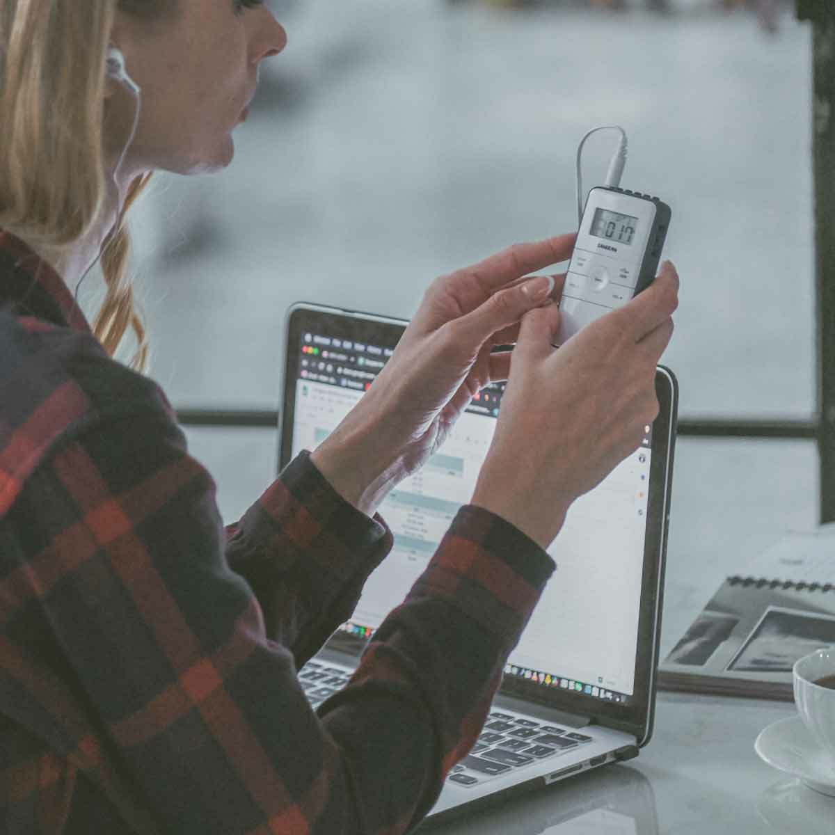 Kobieta używająca laptopa i trzymająca cyfrowy dyktafon.
