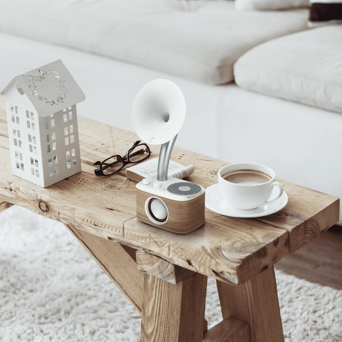 Drewniana ławka z głośnikiem, filiżanką kawy, małym domkiem i okularami.