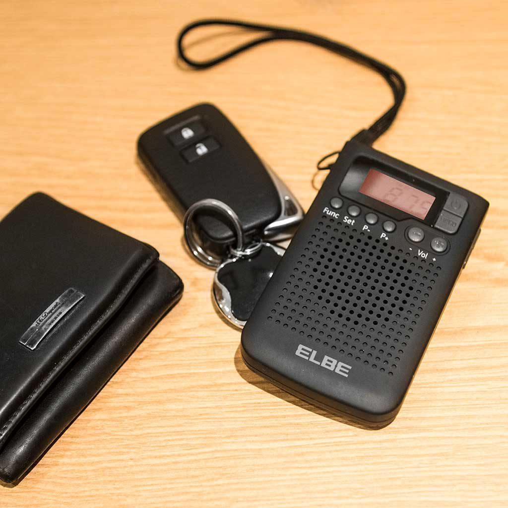 Czarne radio, kluczyk do samochodu i portfel na drewnianym stole. Radio wyświetla cyfrowy wyświetlacz.