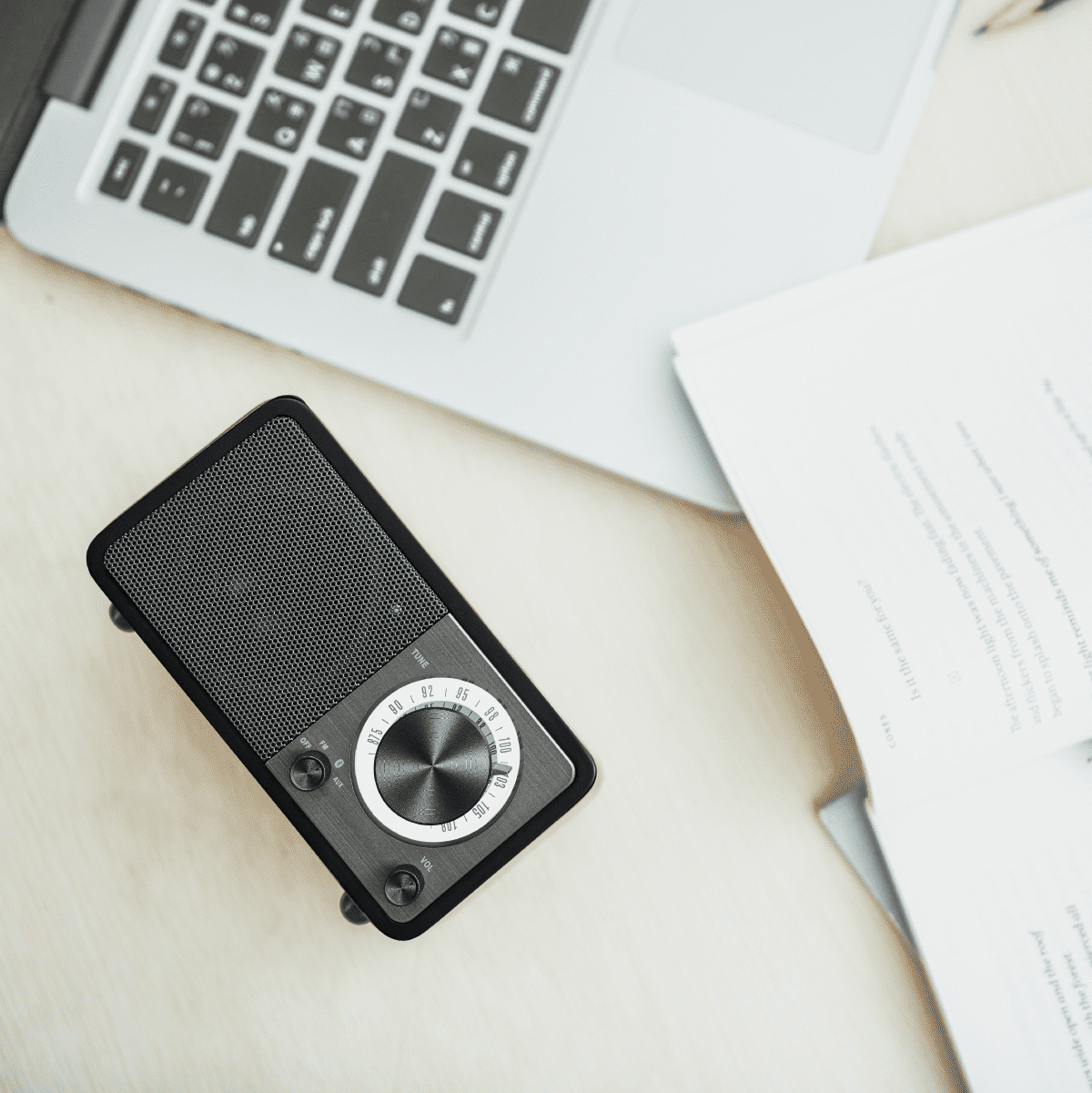 Małe czarne radio, laptop i dokumenty na jasnej drewnianej powierzchni.
