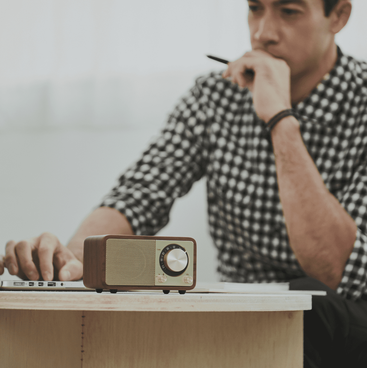 Mężczyzna siedzi przy biurku z laptopem i radiem retro. Radio jest brązowe i złote.