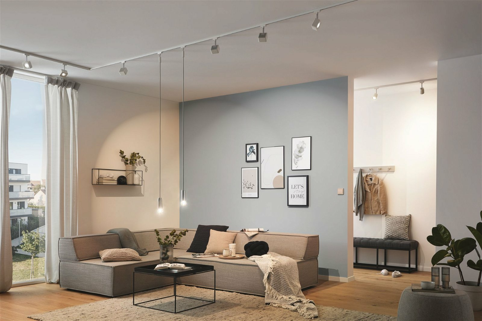 Ein modernes Wohnzimmer mit grauem Sofa, Kunstwerken und Schienenbeleuchtung.