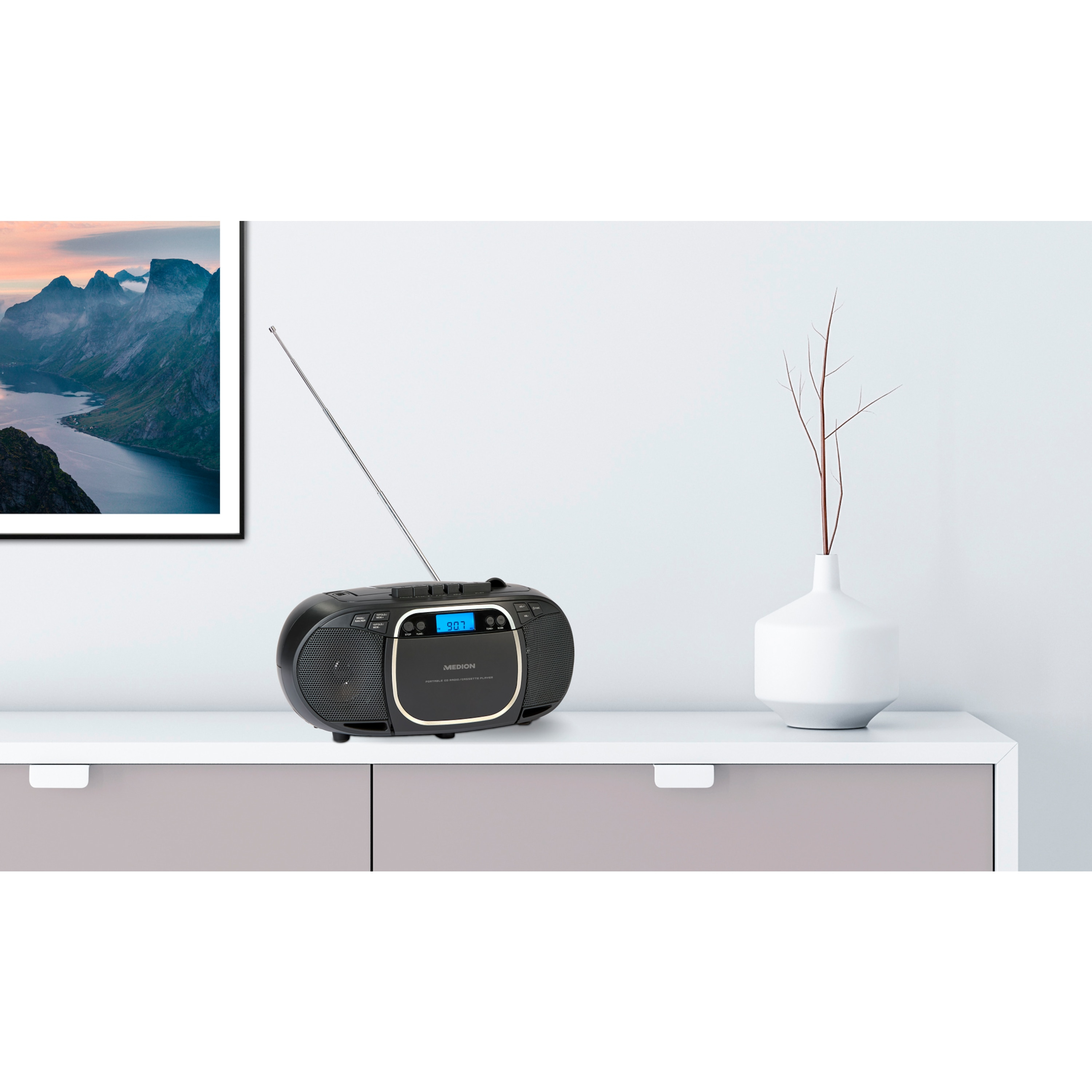 Schwarze Boombox auf weißer Oberfläche. Ein Bild und eine Vase im Hintergrund.