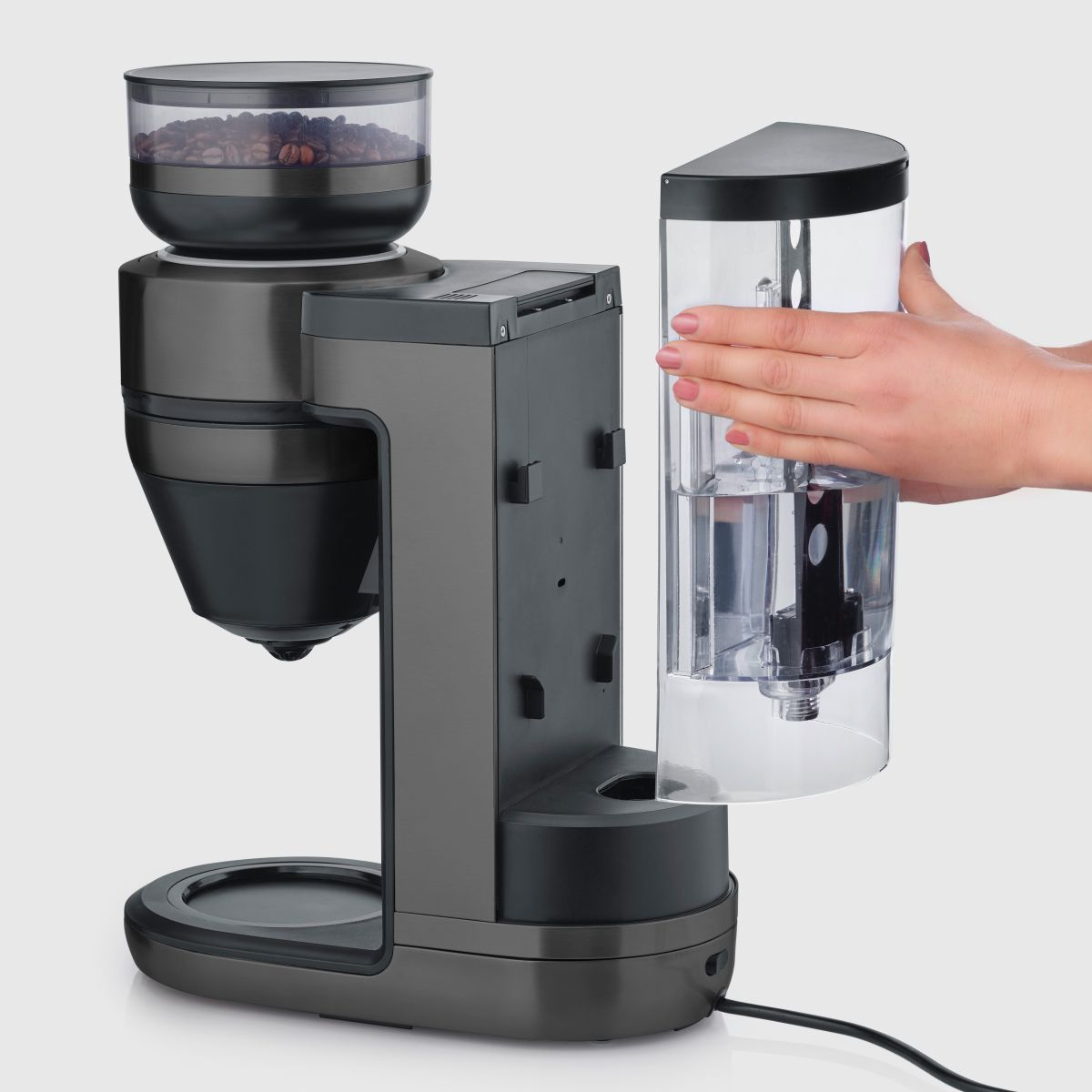 Una cafetera gris oscura con tolva de granos y un depósito de agua siendo retirado.