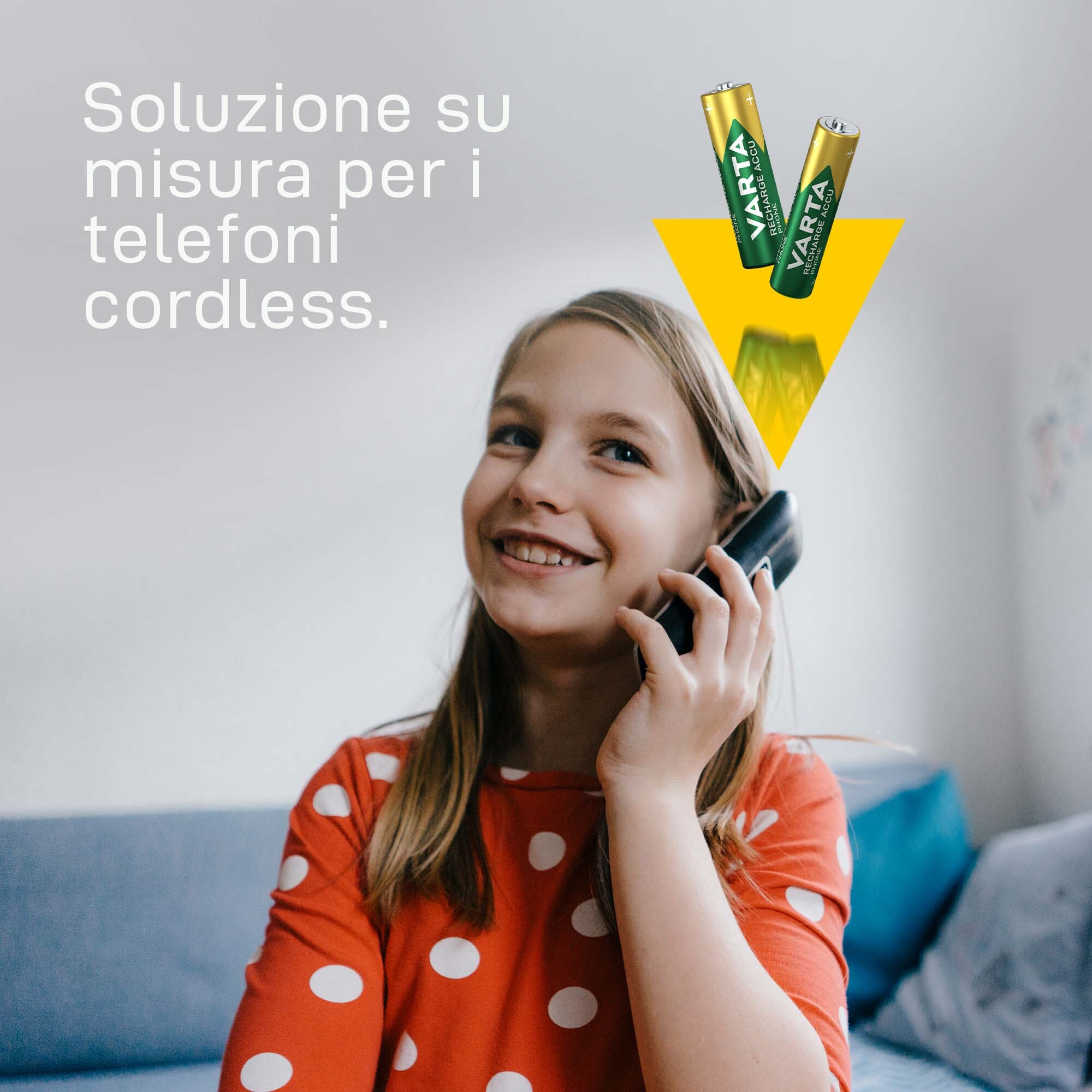 Ein Mädchen in einem roten Polka-Dot-Shirt telefoniert mit einem schnurlosen Telefon, Batterien in der Nähe.