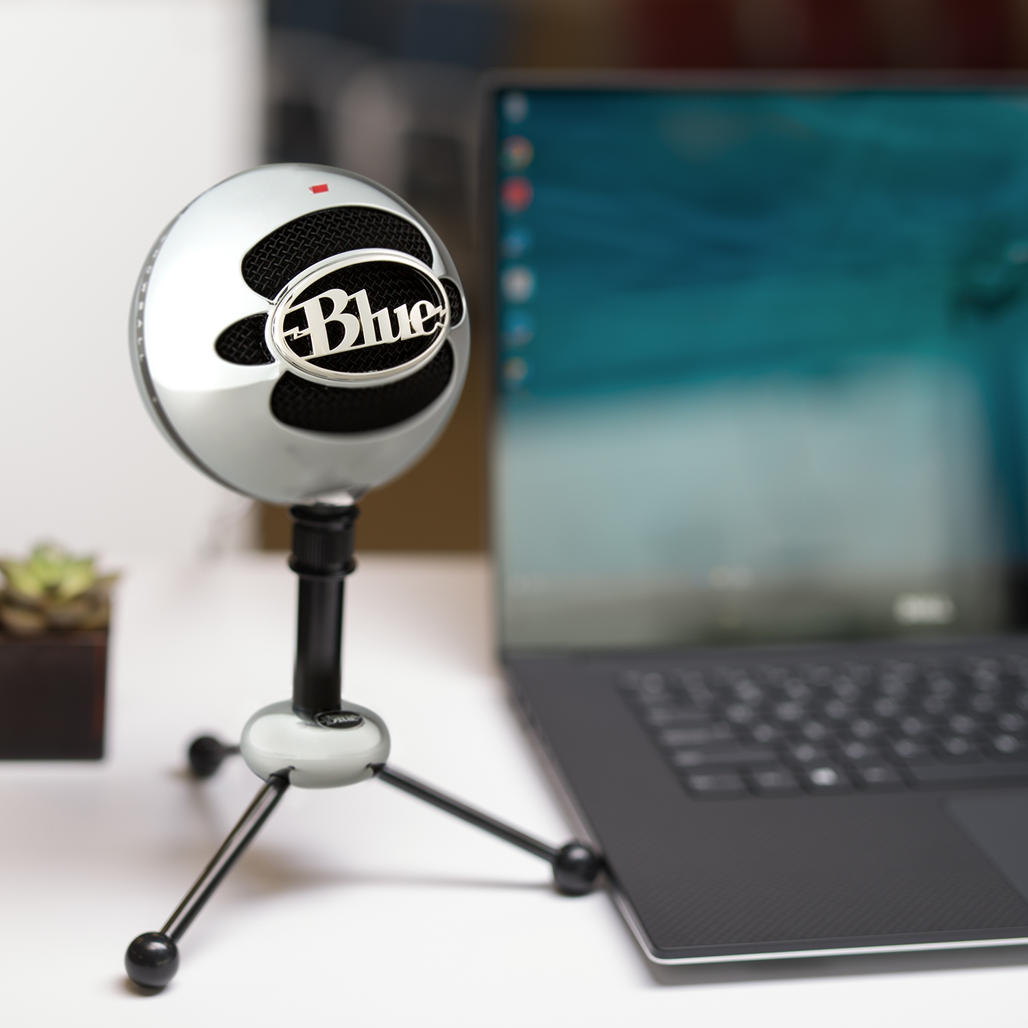 Ein silbernes und schwarzes Blue Yeti Mikrofon auf einem Ständer in der Nähe eines Laptops.