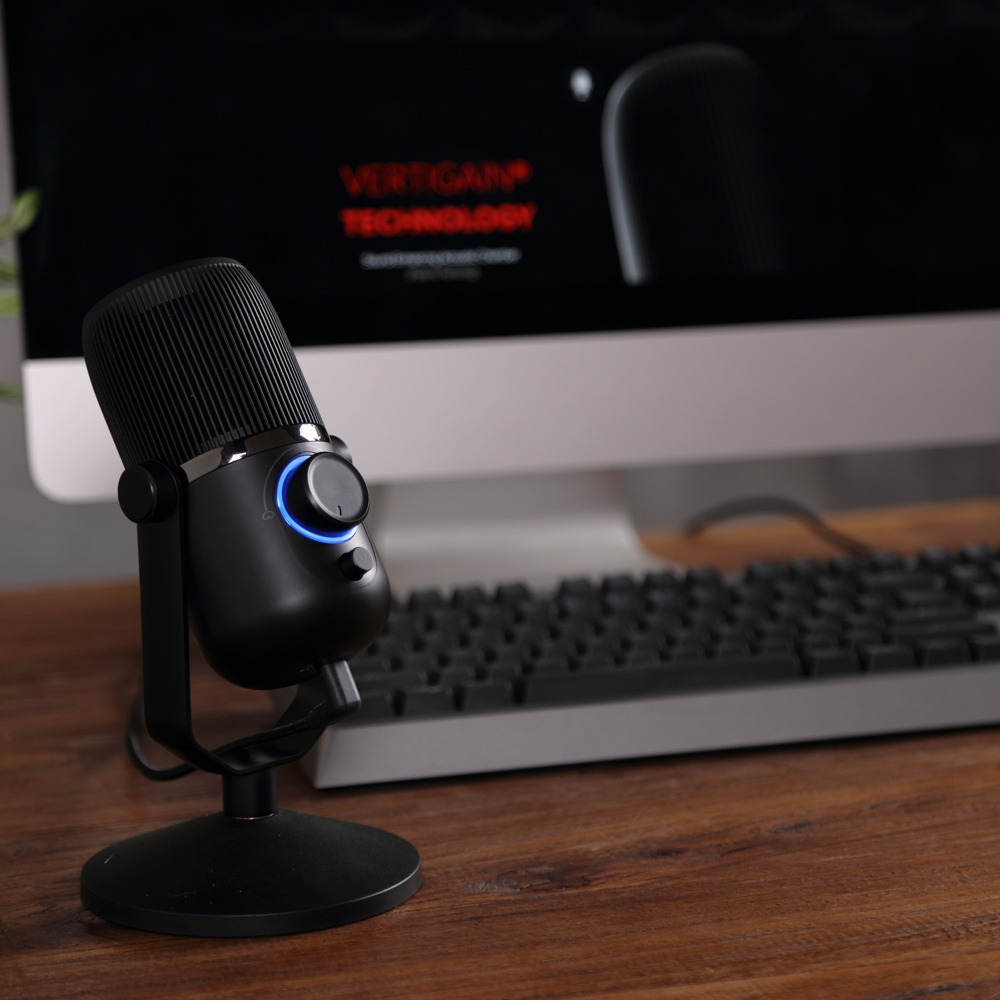 Un micrófono negro sobre un soporte frente a un monitor que muestra el logotipo de Vertigan Technology.