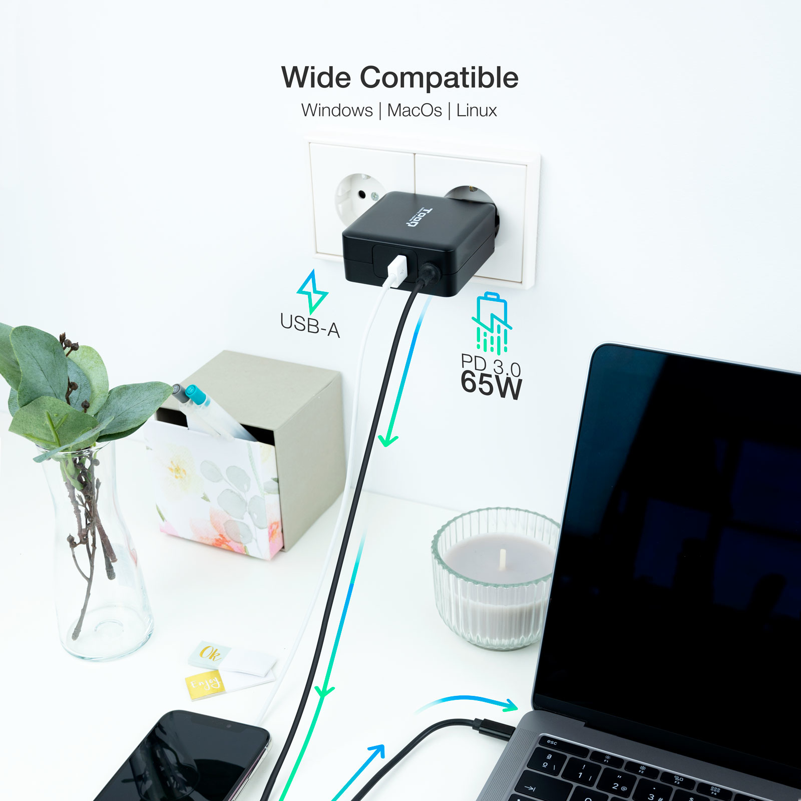 Configuración de escritorio blanca con un portátil cargando. Hay un adaptador de corriente y una planta verde.