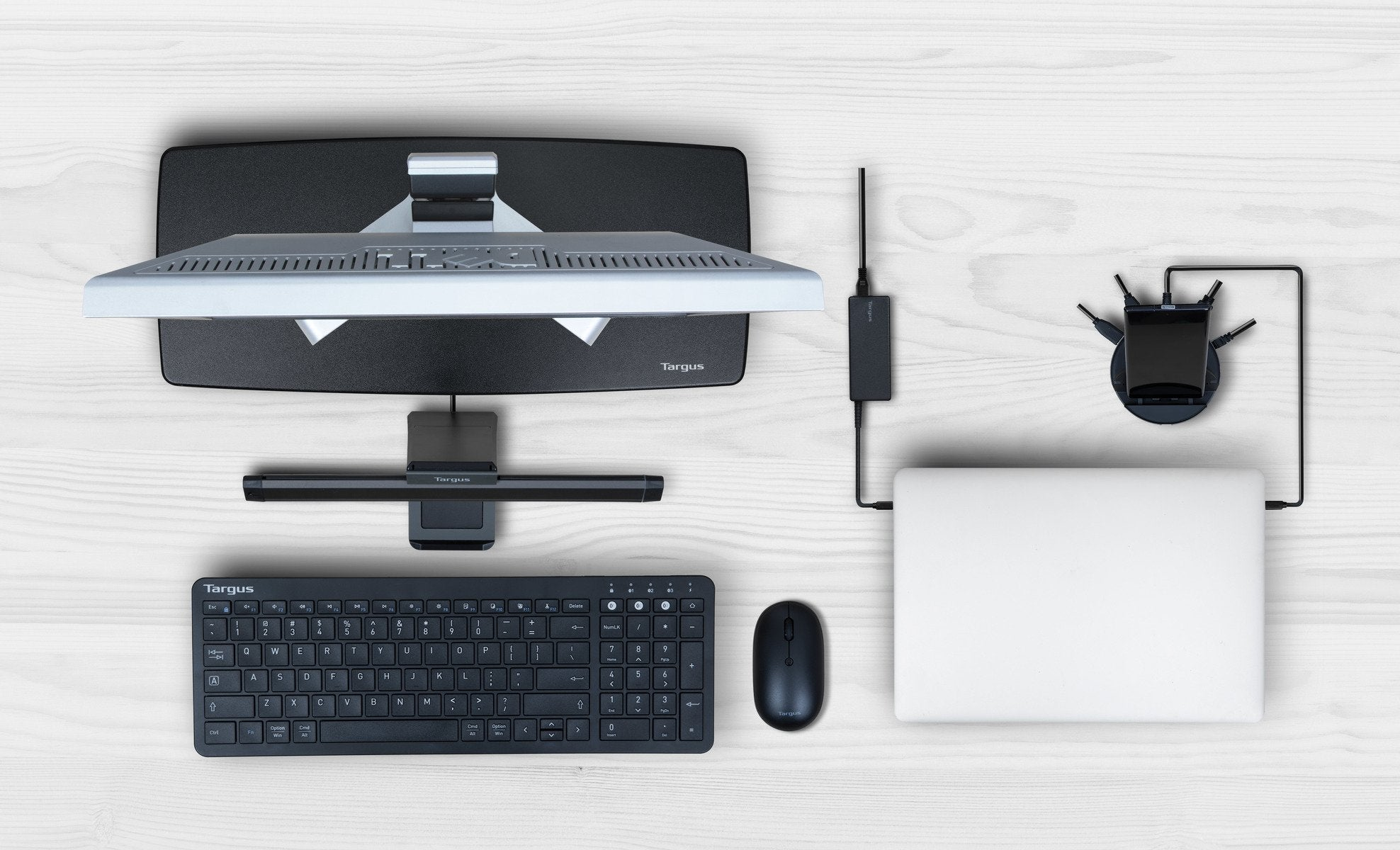 Configurazione desktop con monitor, tastiera, mouse, laptop e altri accessori su una superficie in legno.