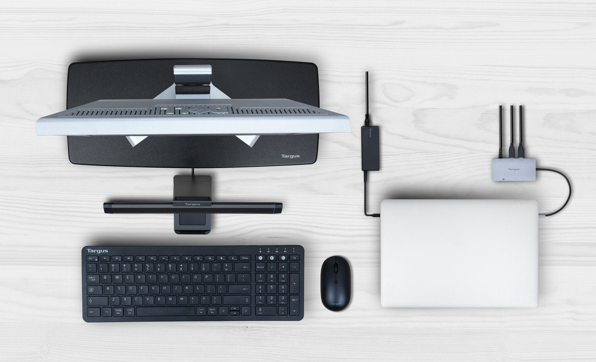 Una vista dall'alto di accessori per computer: monitor, tastiera, mouse, laptop e un hub USB. Superficie in legno bianco.